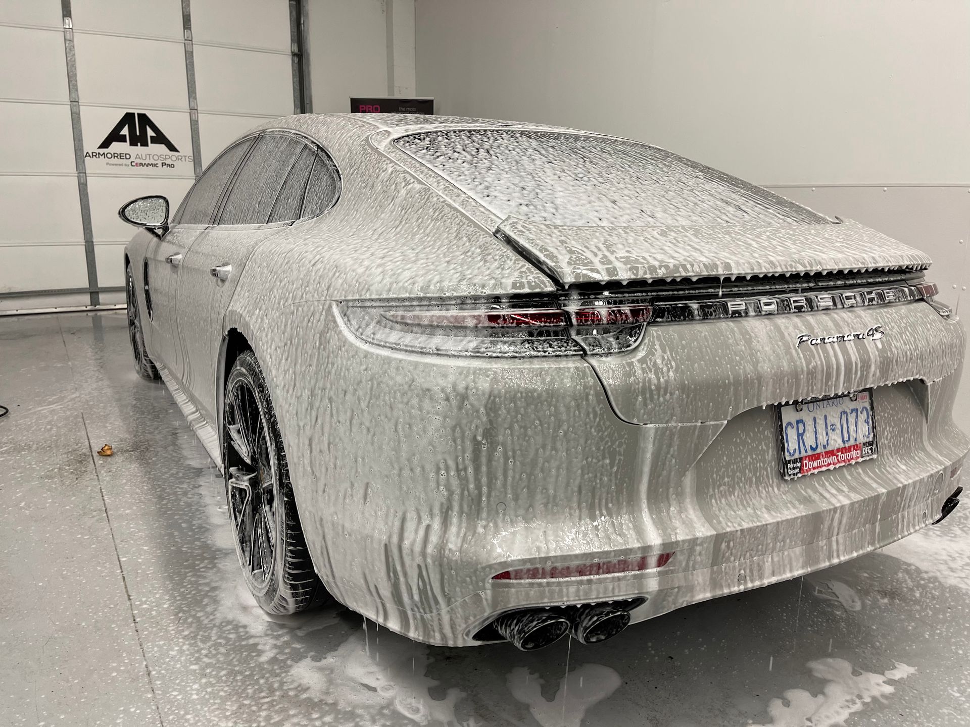 A Porsche Panamera covered in thick white soap suds during a car wash inside a garage.