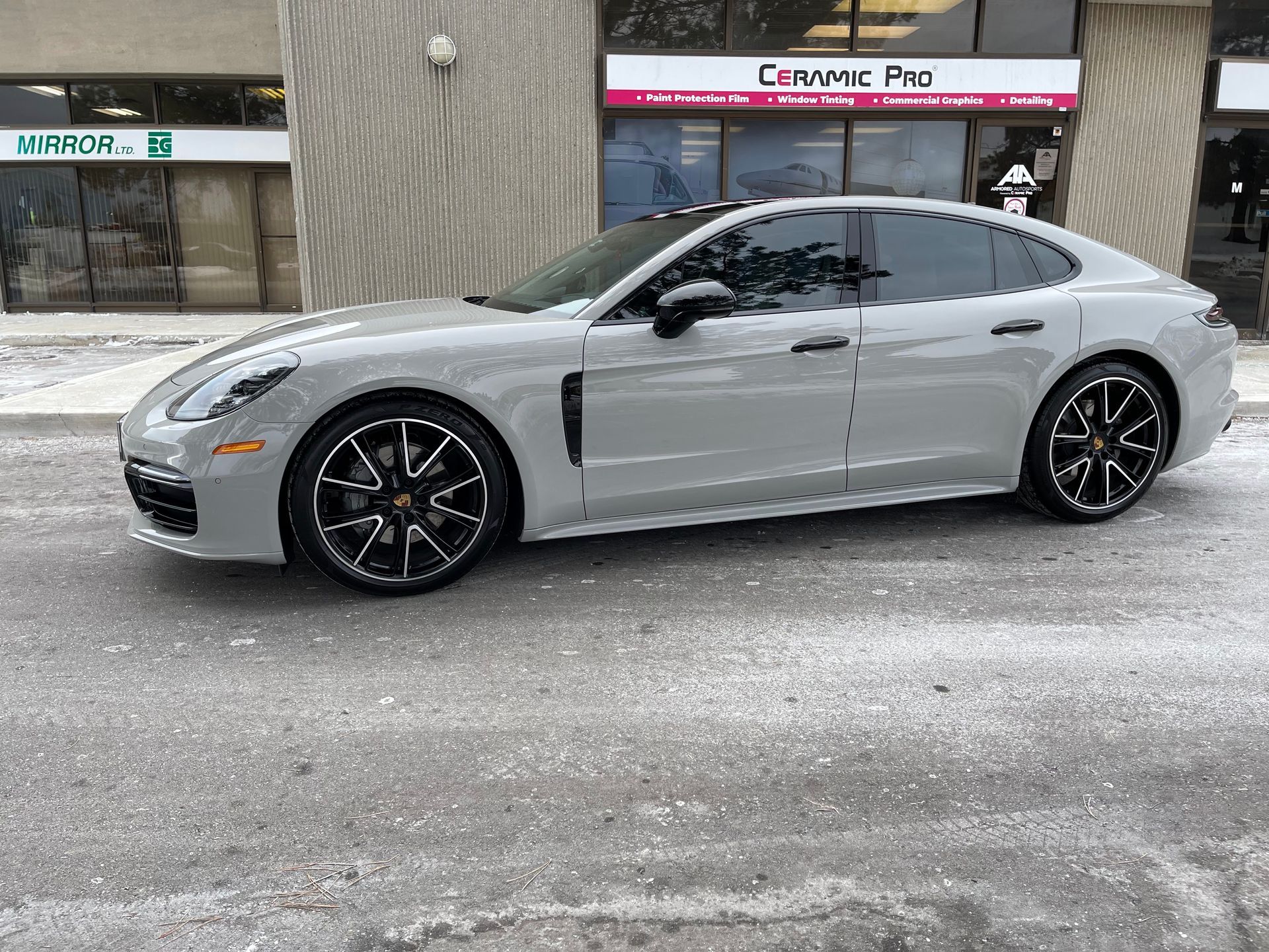 A sleek, grey Porsche Panamera parked in front of a Ceramic Pro automotive shop.