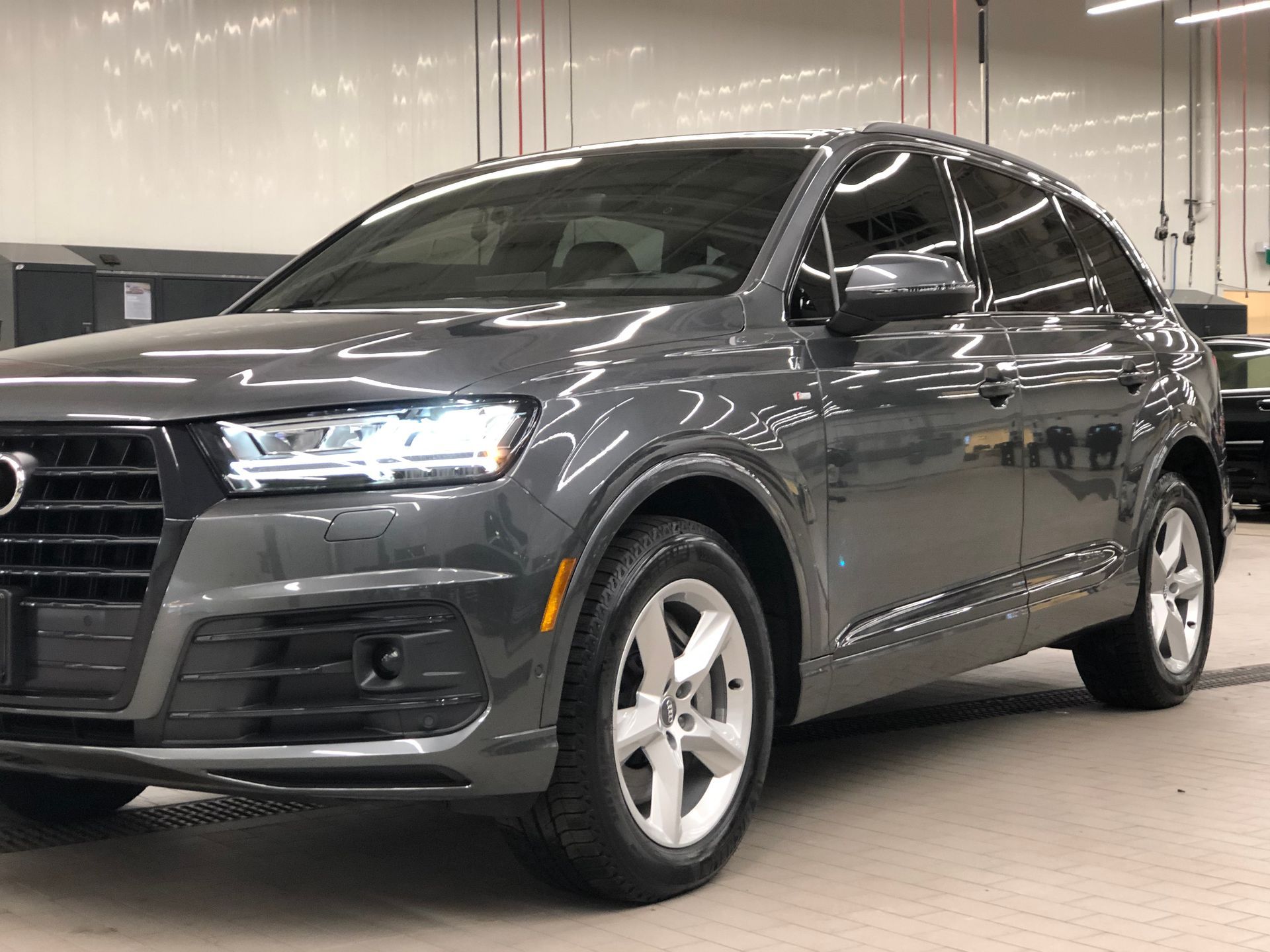 A dark gray Audi Q7 SUV parked inside a garage with bright overhead lighting.