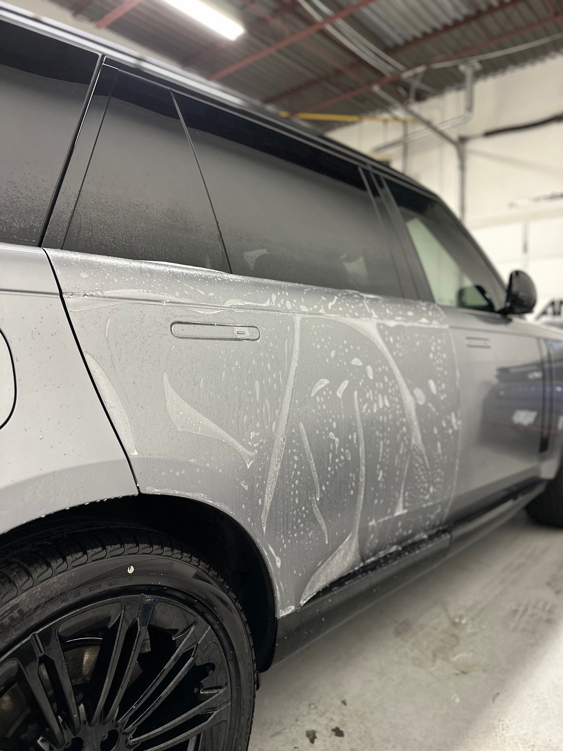 A silver Range Rover side panel covered in white soapy foam inside a workshop.