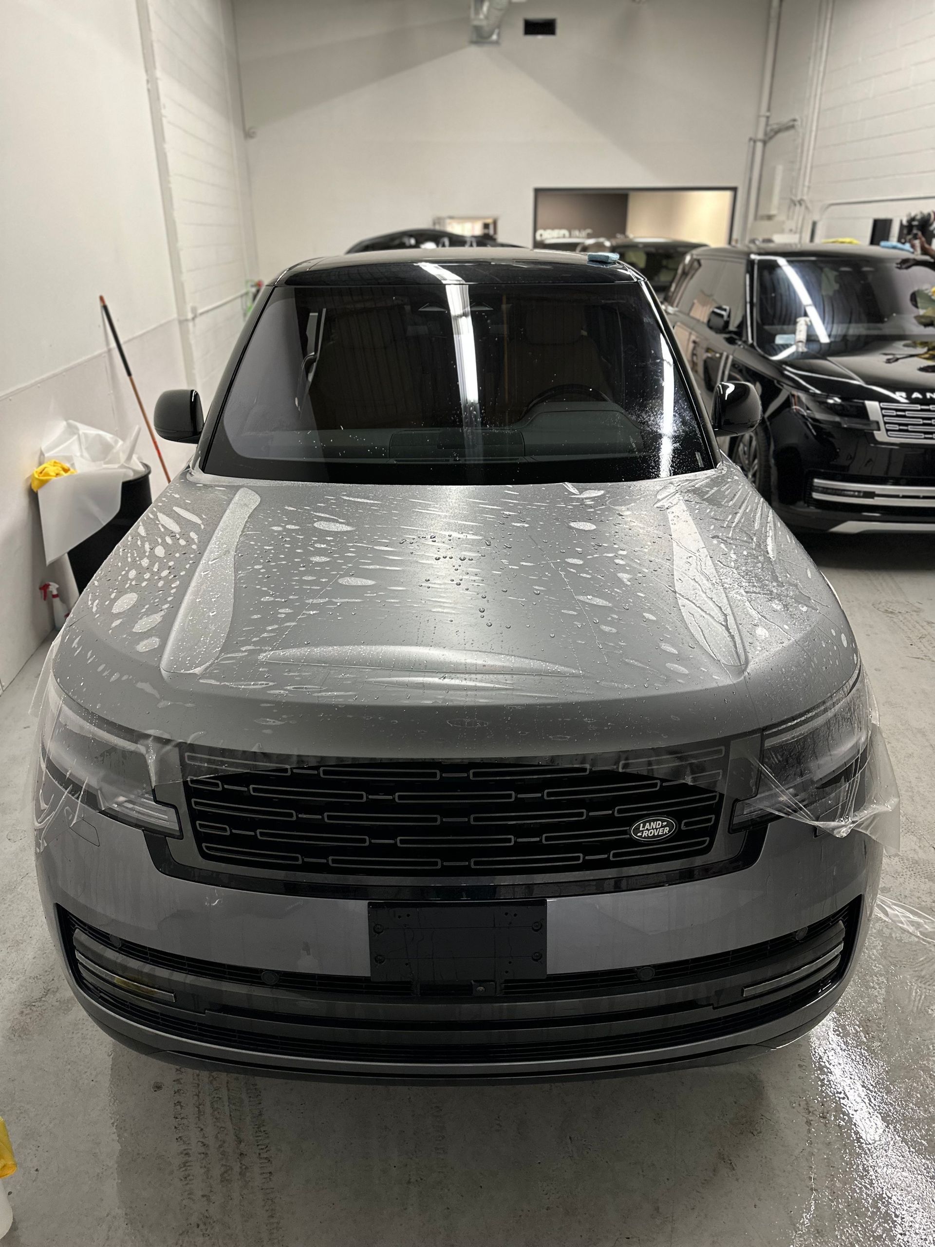 A silver Range Rover parked in a garage, undergoing the installation of a transparent paint protection film.