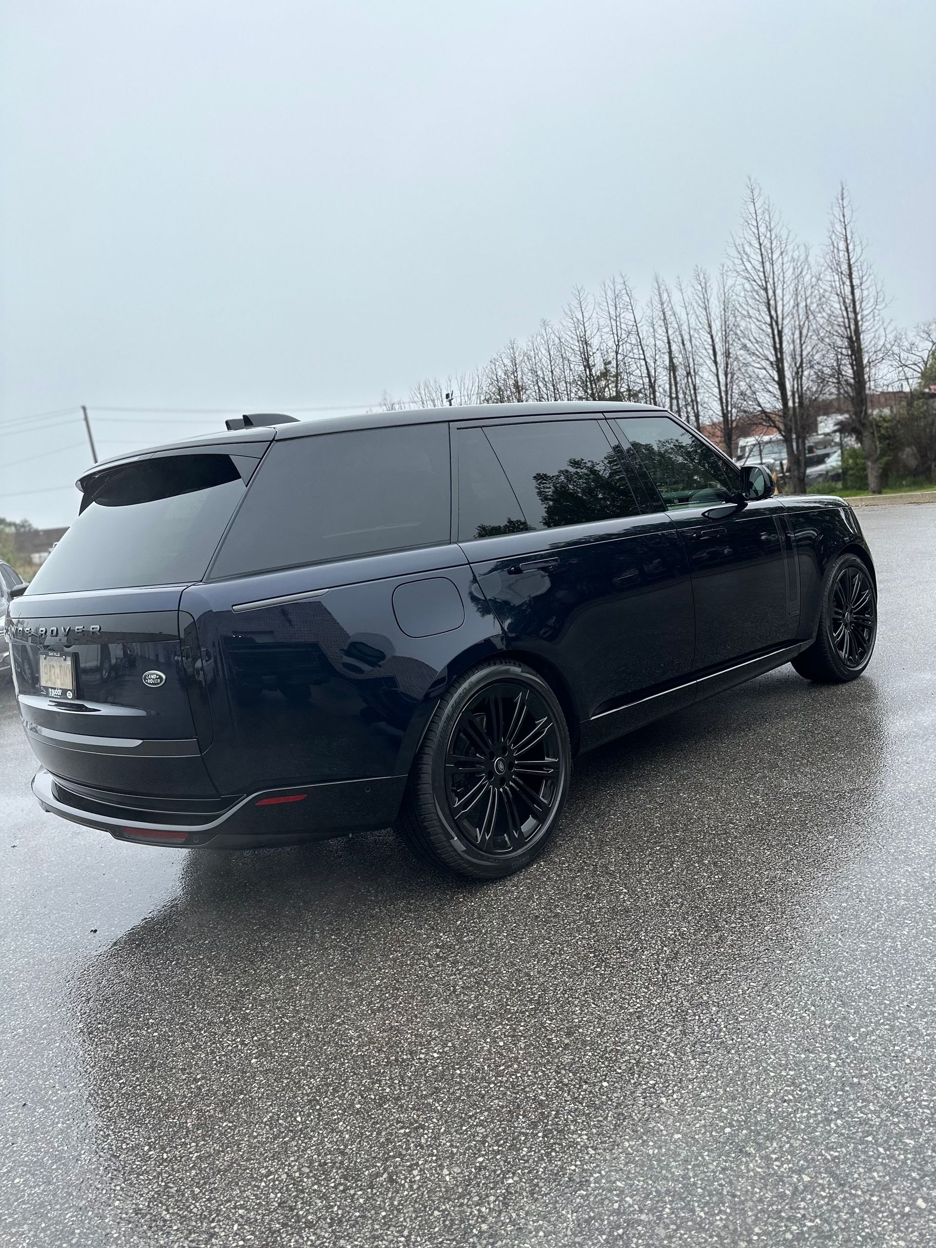 A dark blue Range Rover parked on a wet, gray asphalt surface on a cloudy day.