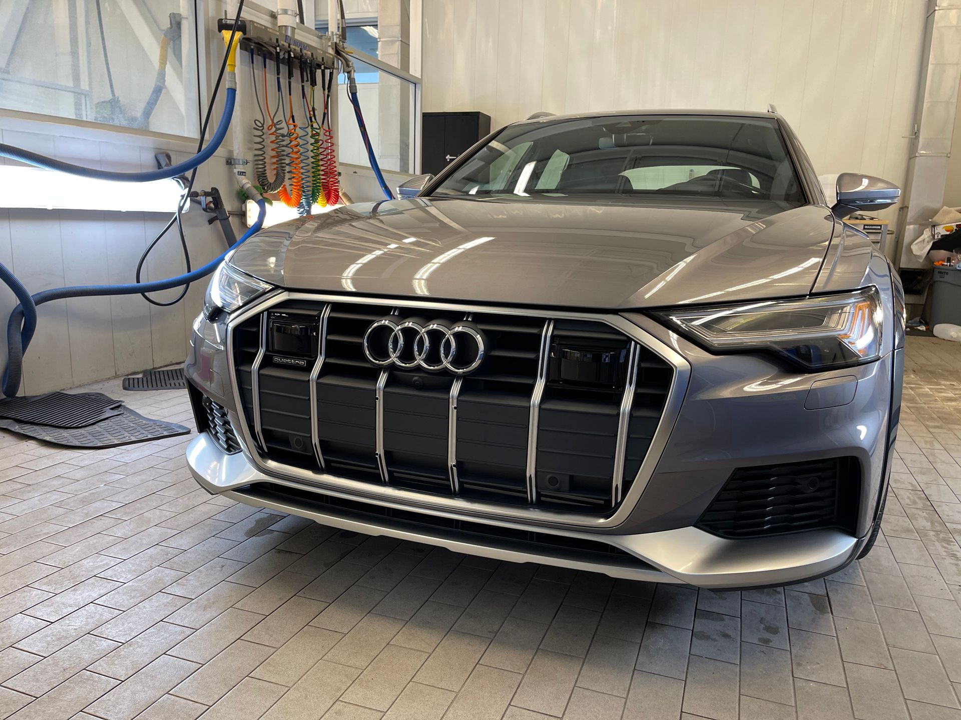 A grey Audi parked in a garage with industrial cleaning equipment visible in the background.