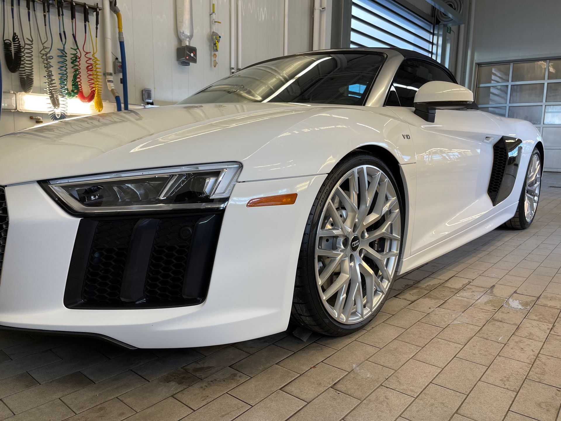 A sleek, white Audi R8 sports car parked on a tiled garage floor.