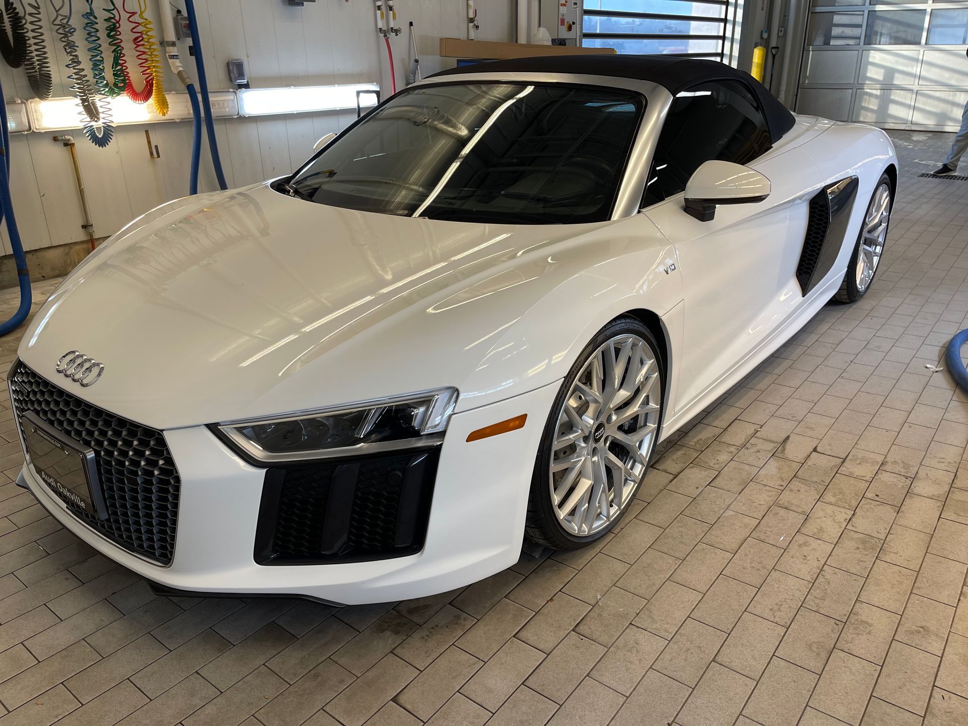 A white Audi R8 convertible parked inside a well-lit car wash bay with tiled flooring.
