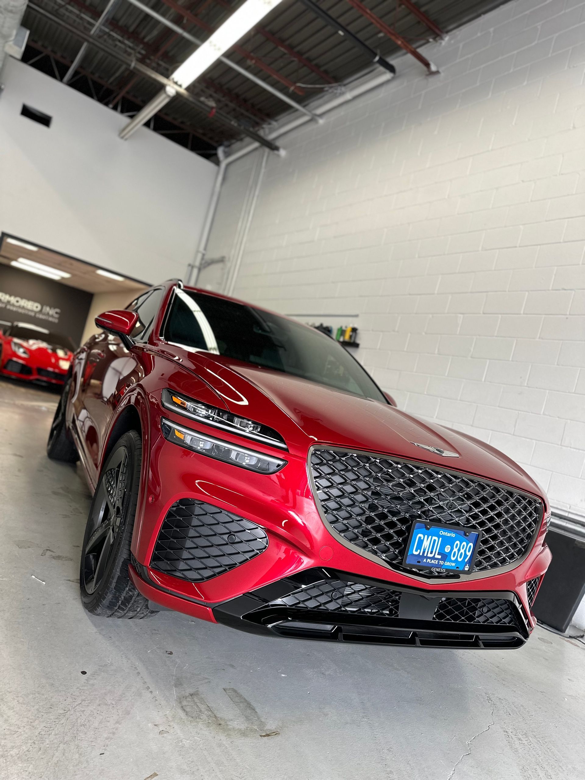 A glossy red Genesis GV70 SUV parked at a slight angle inside a brightly lit professional garage.