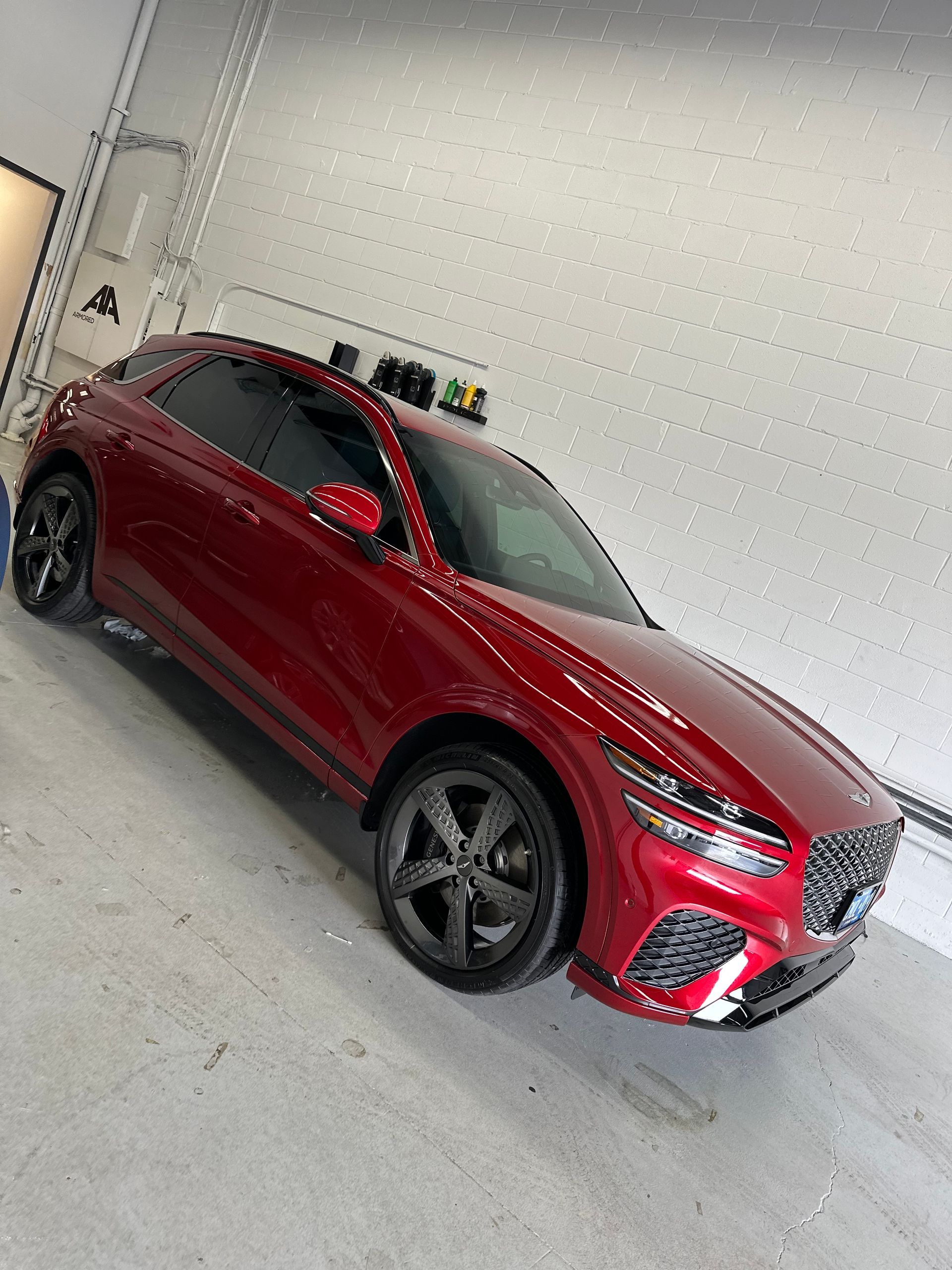 A glossy red Genesis luxury SUV parked at an angle inside a well-lit studio with a light grey floor and wall.