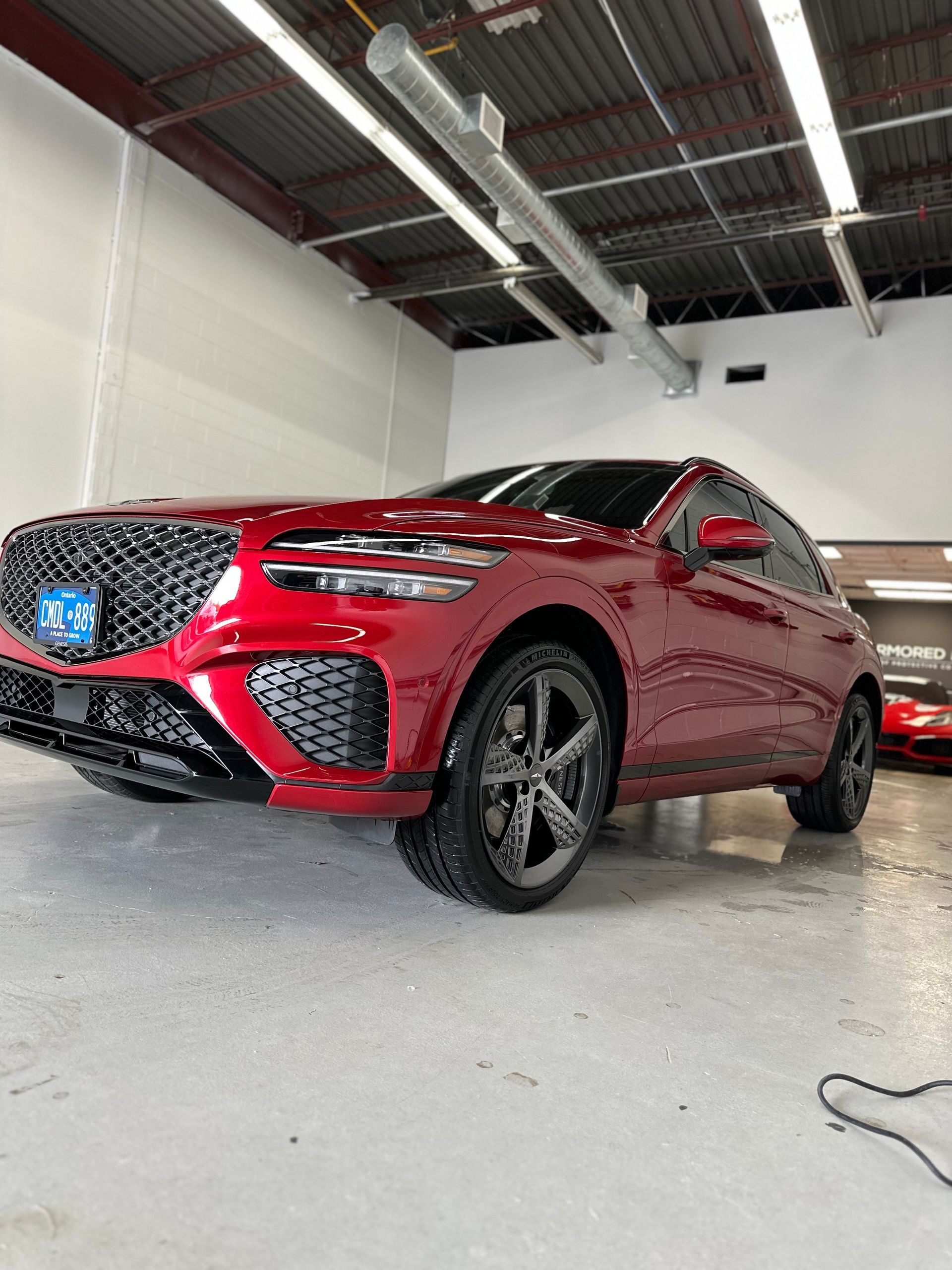 A metallic red Genesis SUV parked inside a brightly lit, industrial-style garage.