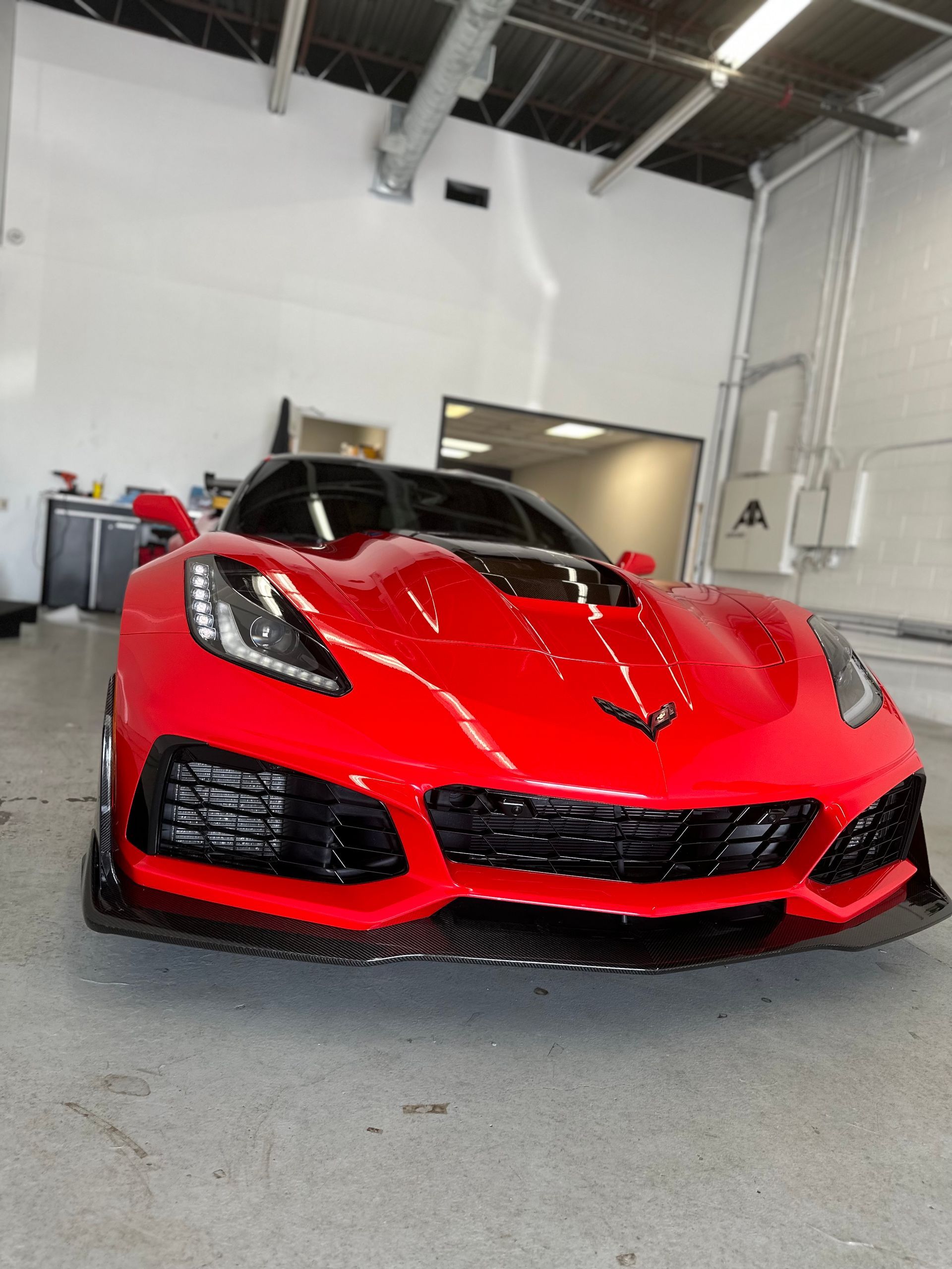 A bright red Chevrolet Corvette ZR1 parked inside a garage, featuring a black carbon fiber front splitter and trim.