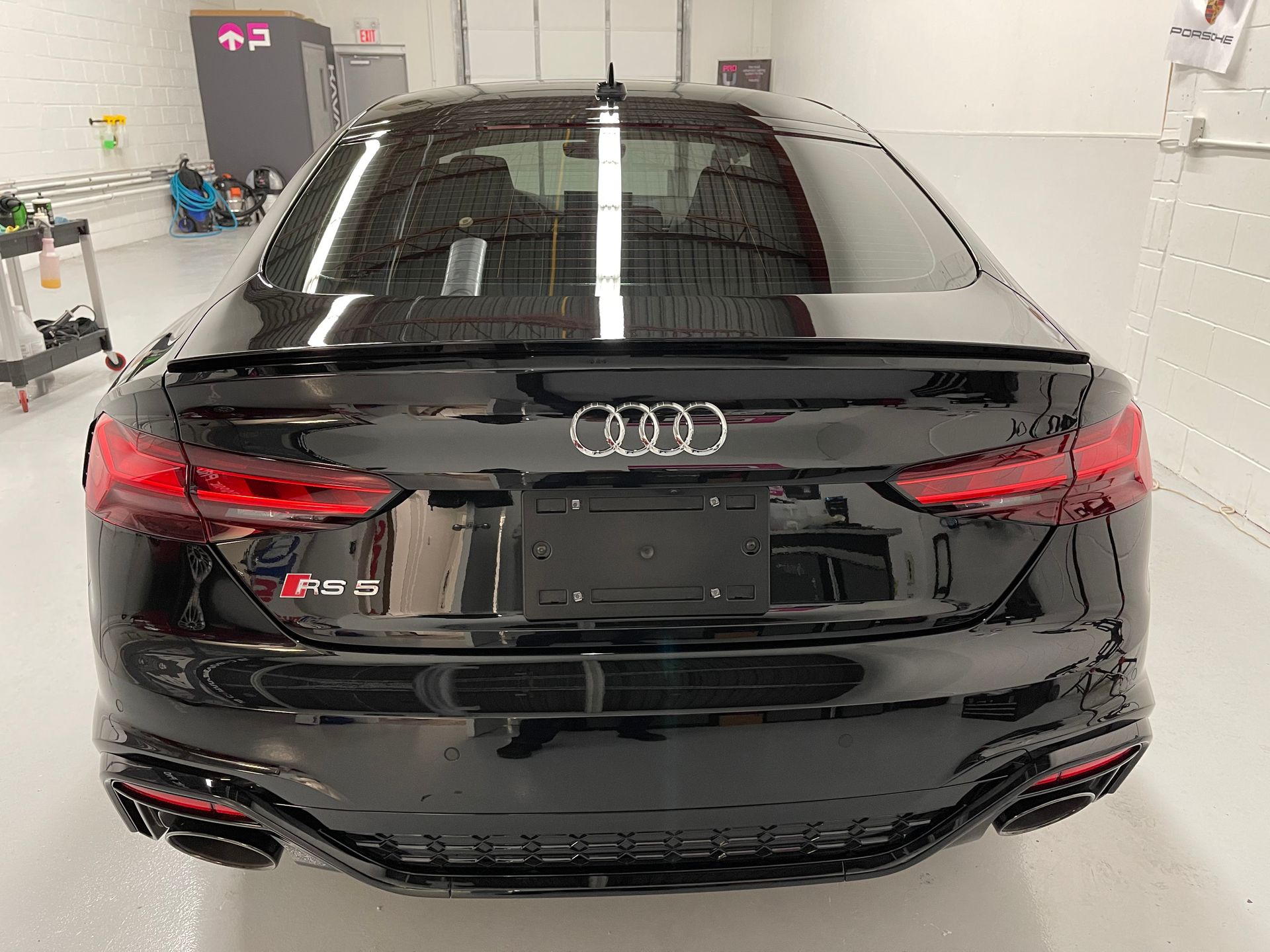 Rear view of a shiny black Audi RS 5 sedan parked inside a brightly lit garage.