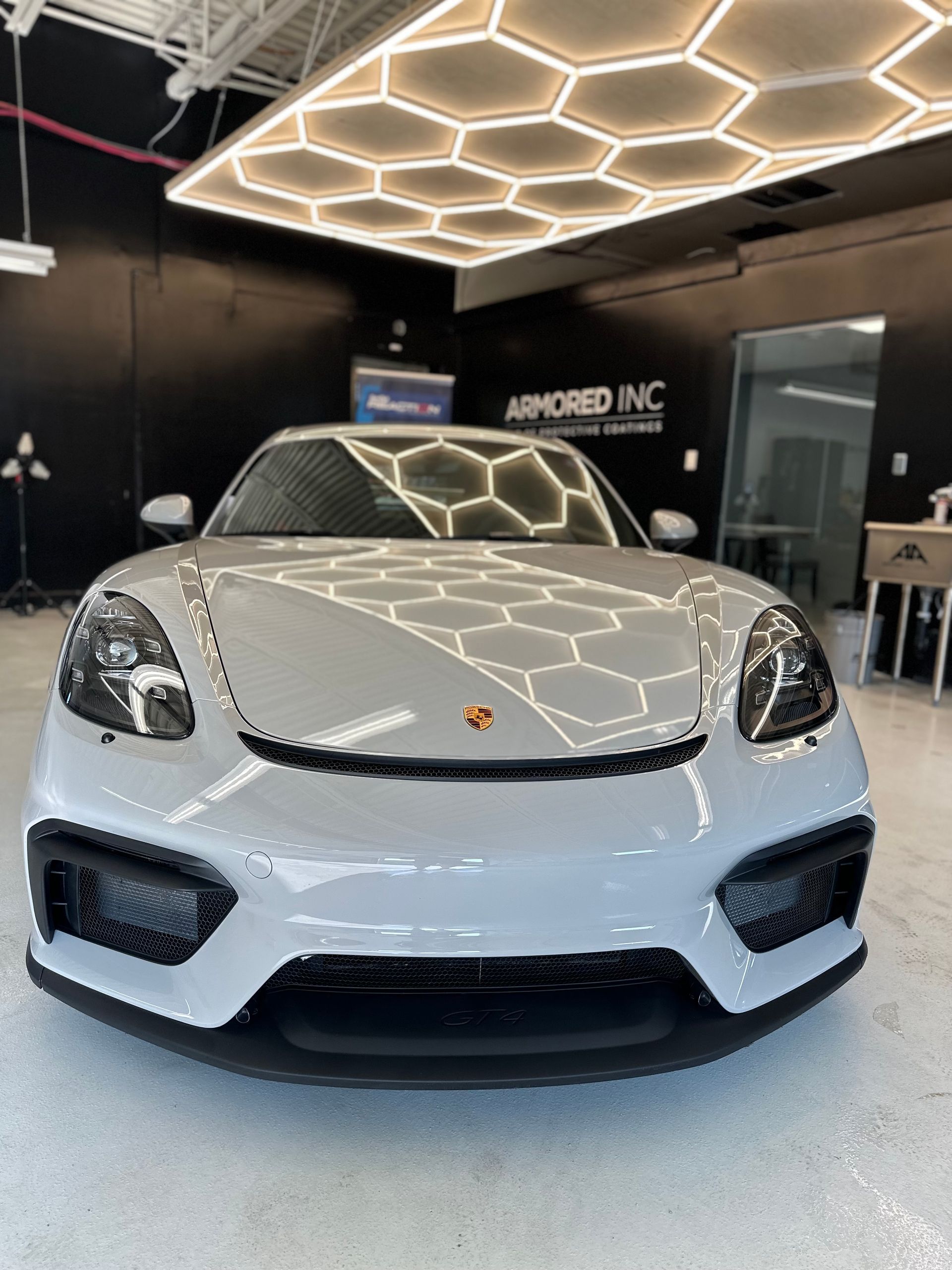 A light grey Porsche sports car parked inside a studio with hexagon-shaped overhead lighting.