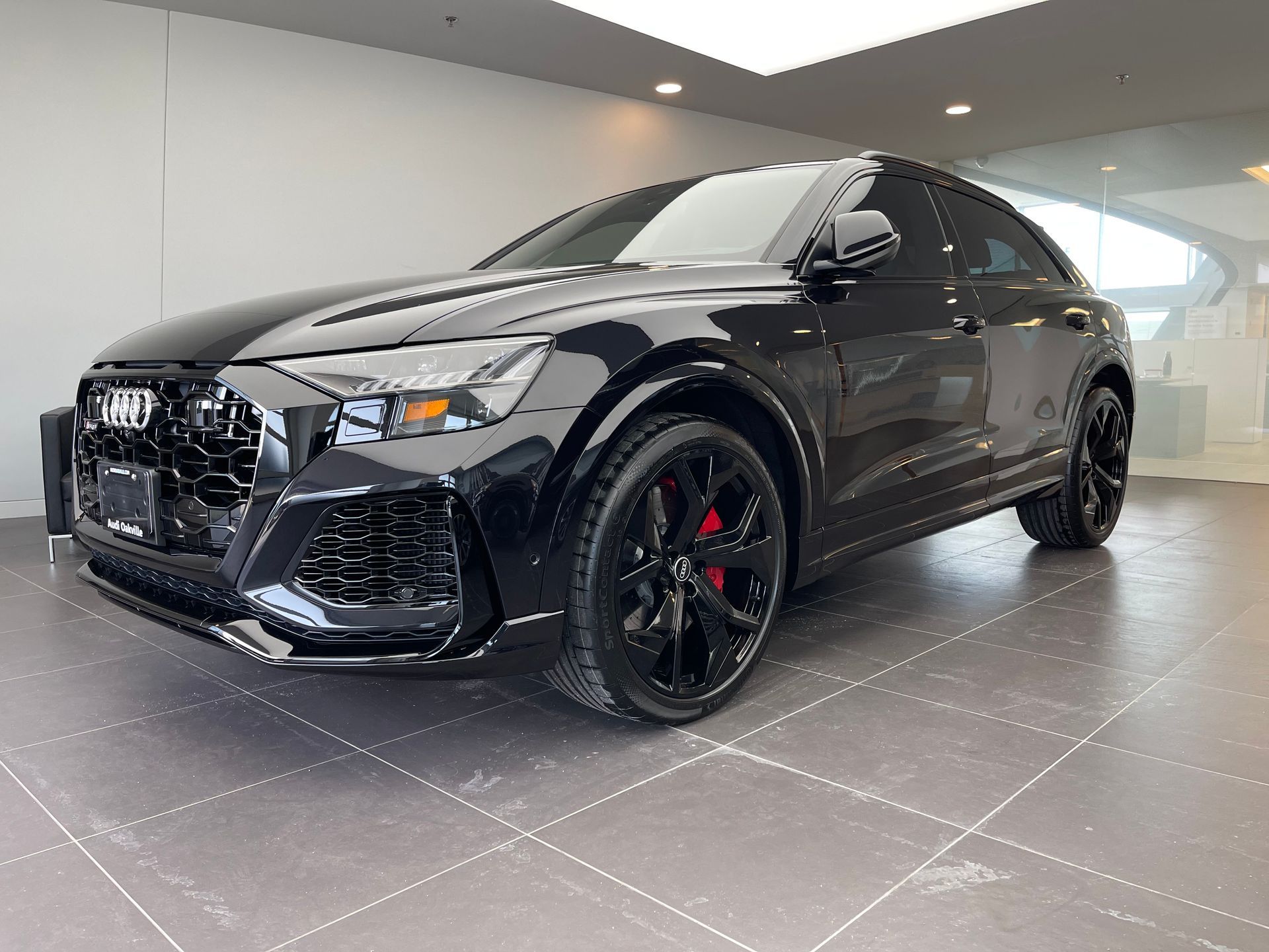 A black Audi RS Q8 SUV parked inside a bright, modern dealership showroom with tiled flooring.
