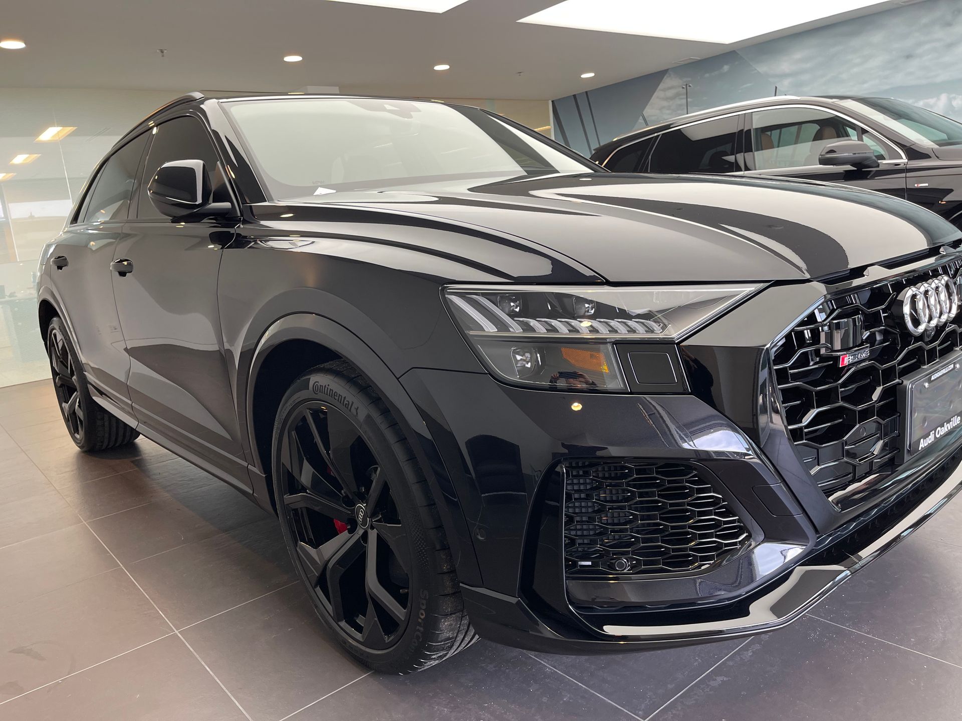 A glossy black Audi RS Q8 SUV parked inside a well-lit showroom with large wheels and an aggressive front grille.