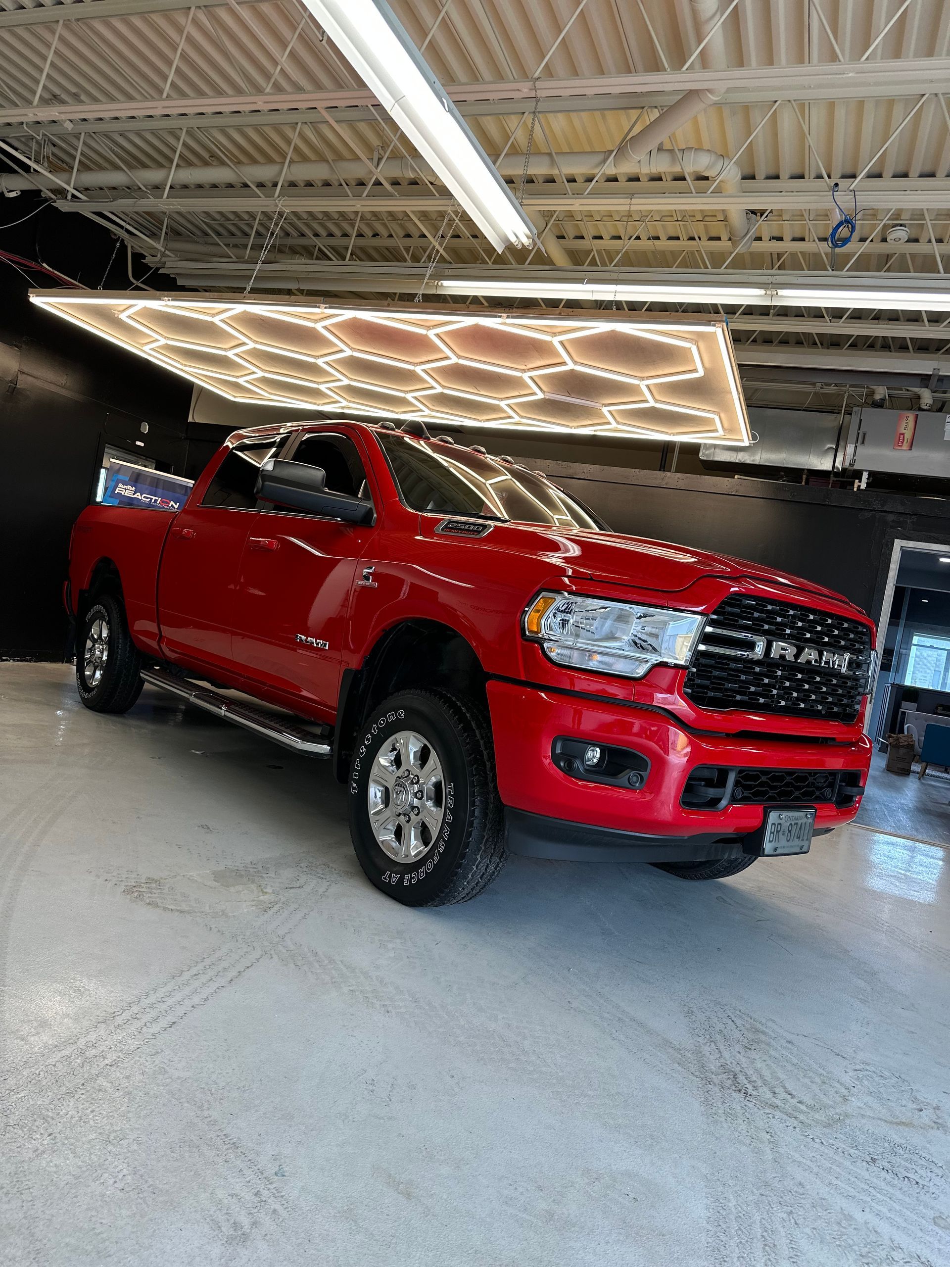 A bright red Ram pickup truck parked in an indoor showroom with a hexagonal-patterned LED ceiling light panel above.