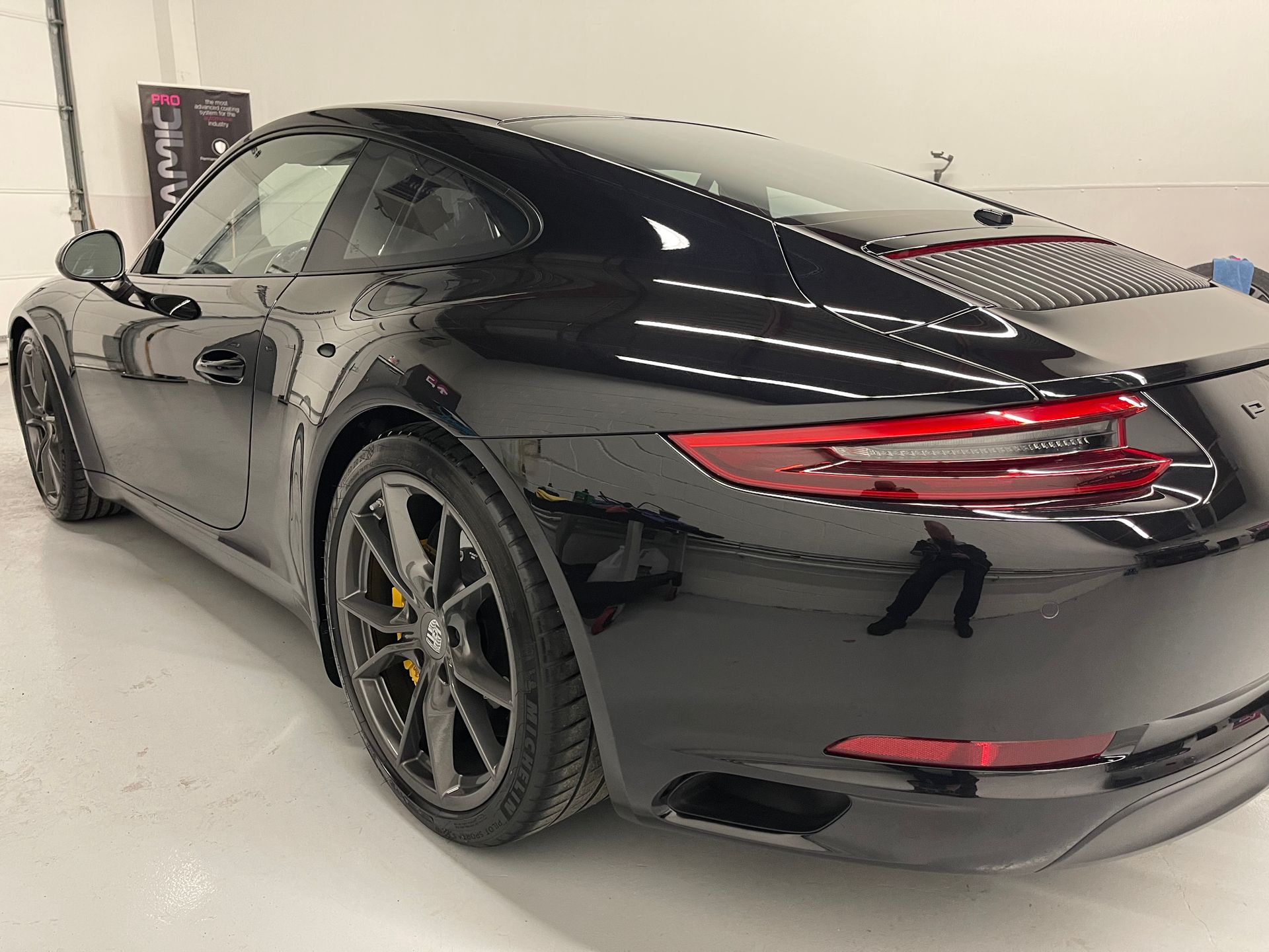 A black Porsche 911 coupe parked in a bright, clean garage, seen from a rear three-quarter angle.