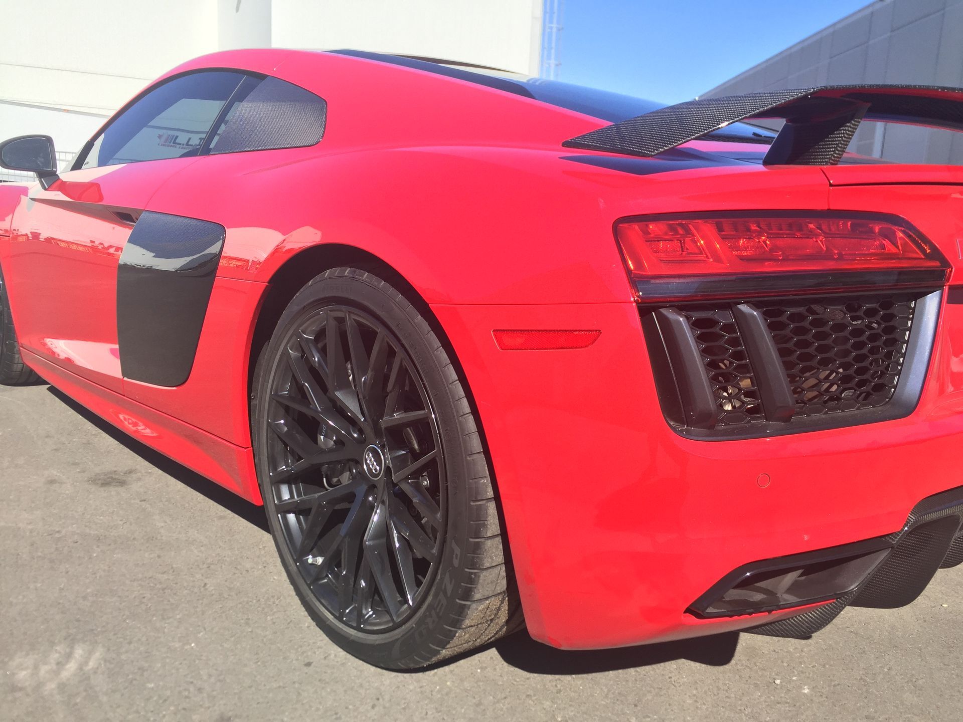 A bright red Audi R8 sports car parked outdoors, showing the rear quarter panel, black alloy wheel, and rear light.