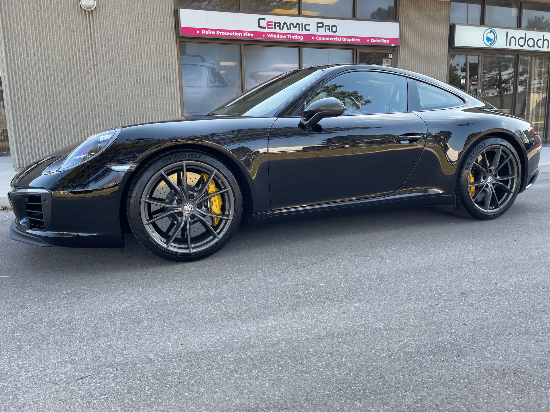 A sleek, glossy black Porsche sports car parked in front of a building storefront.
