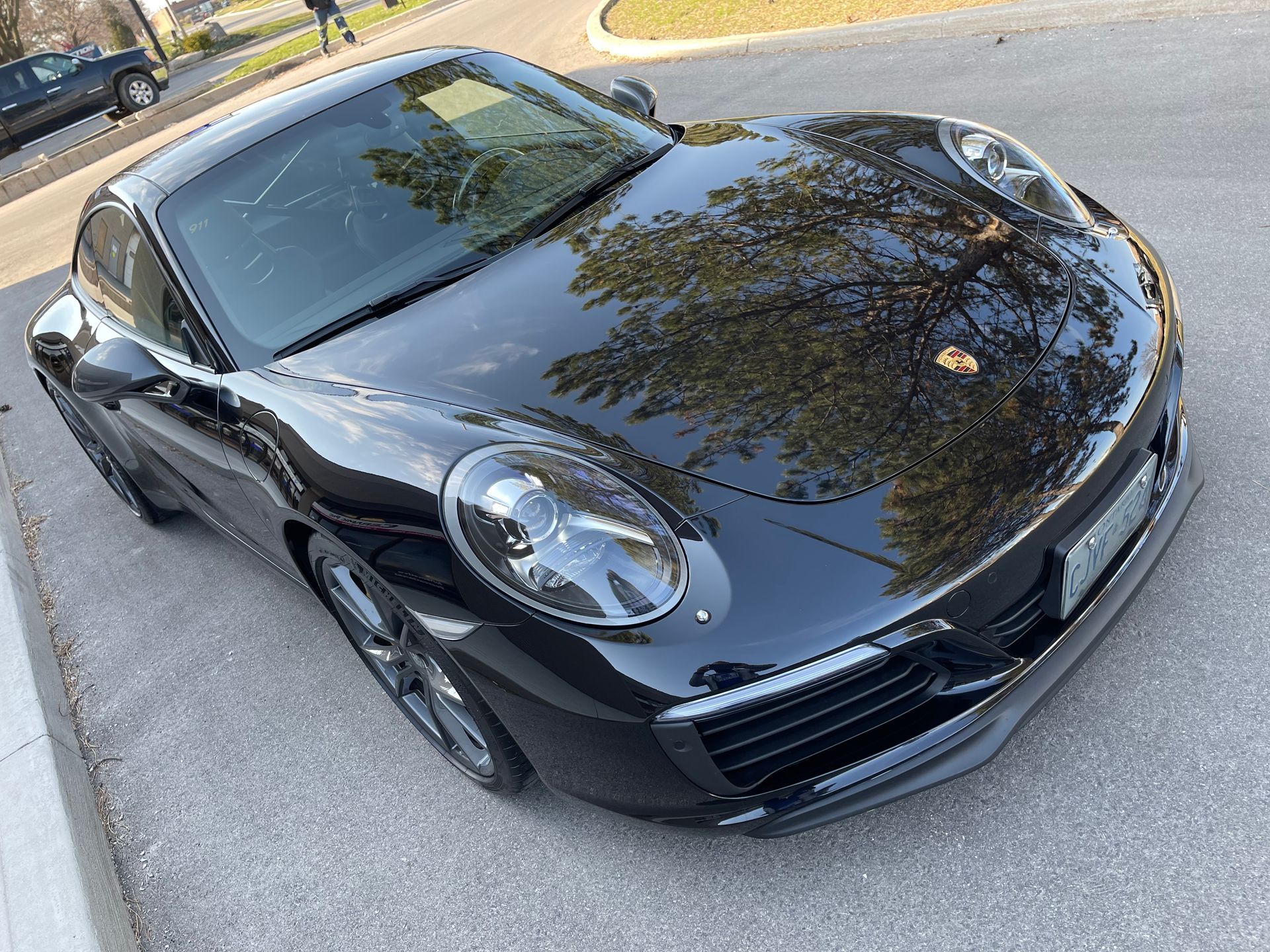 A sleek, black Porsche 911 parked on an asphalt surface, shown from a high-angle front three-quarter view.