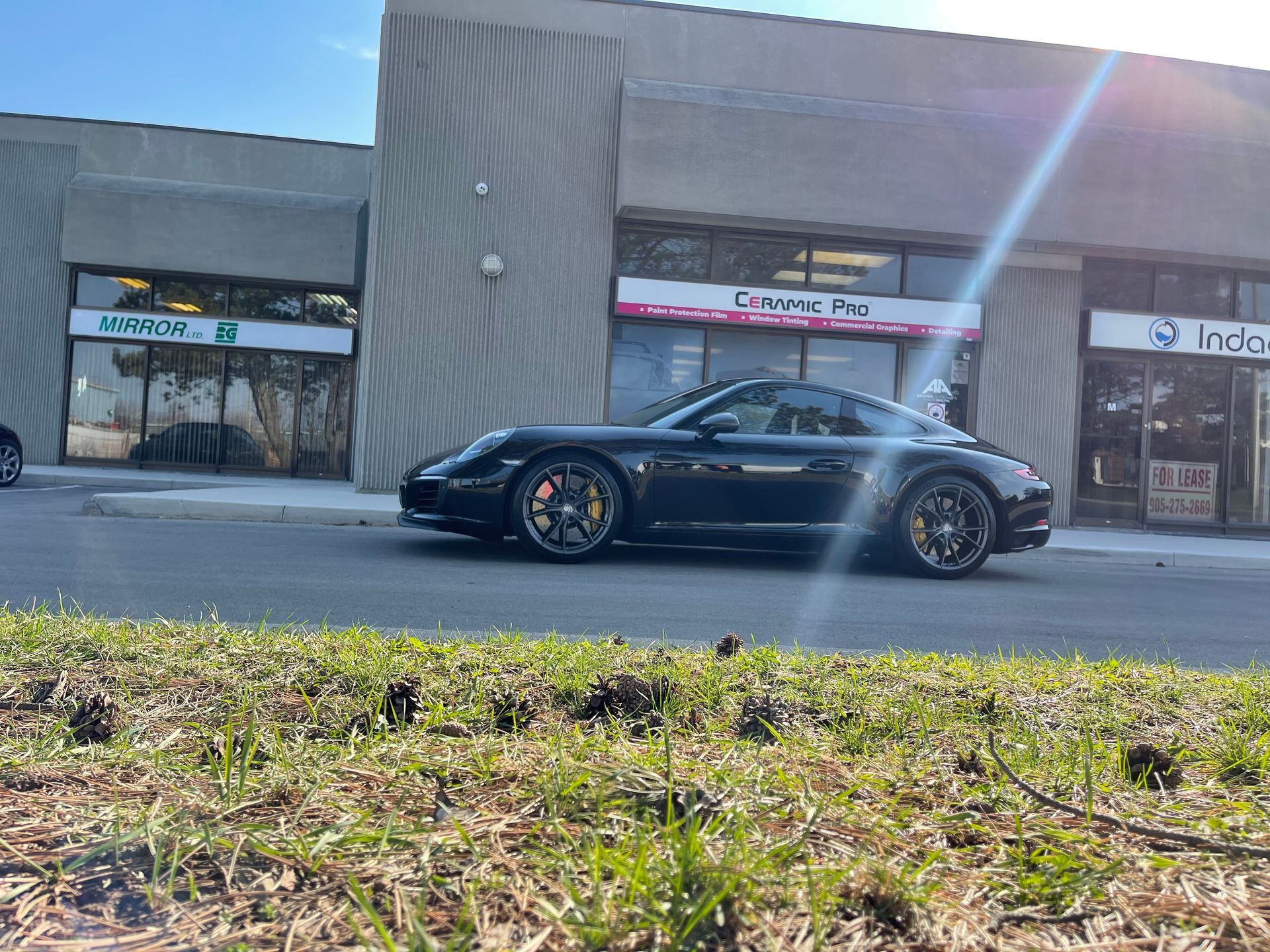 A black Porsche parked in front of commercial storefronts on a sunny day.