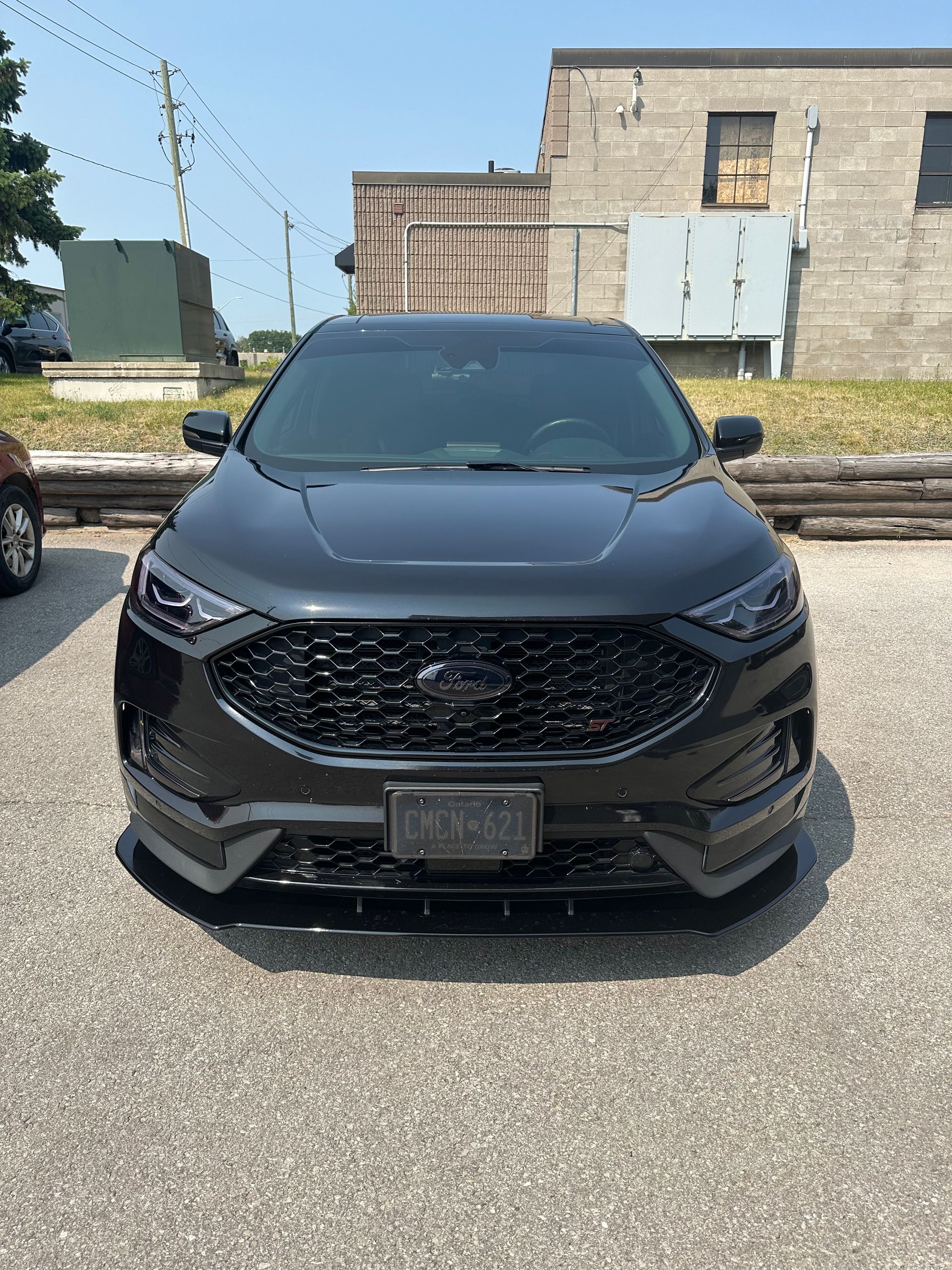A black Ford Edge parked on a gravel lot in front of a brick building on a sunny day.