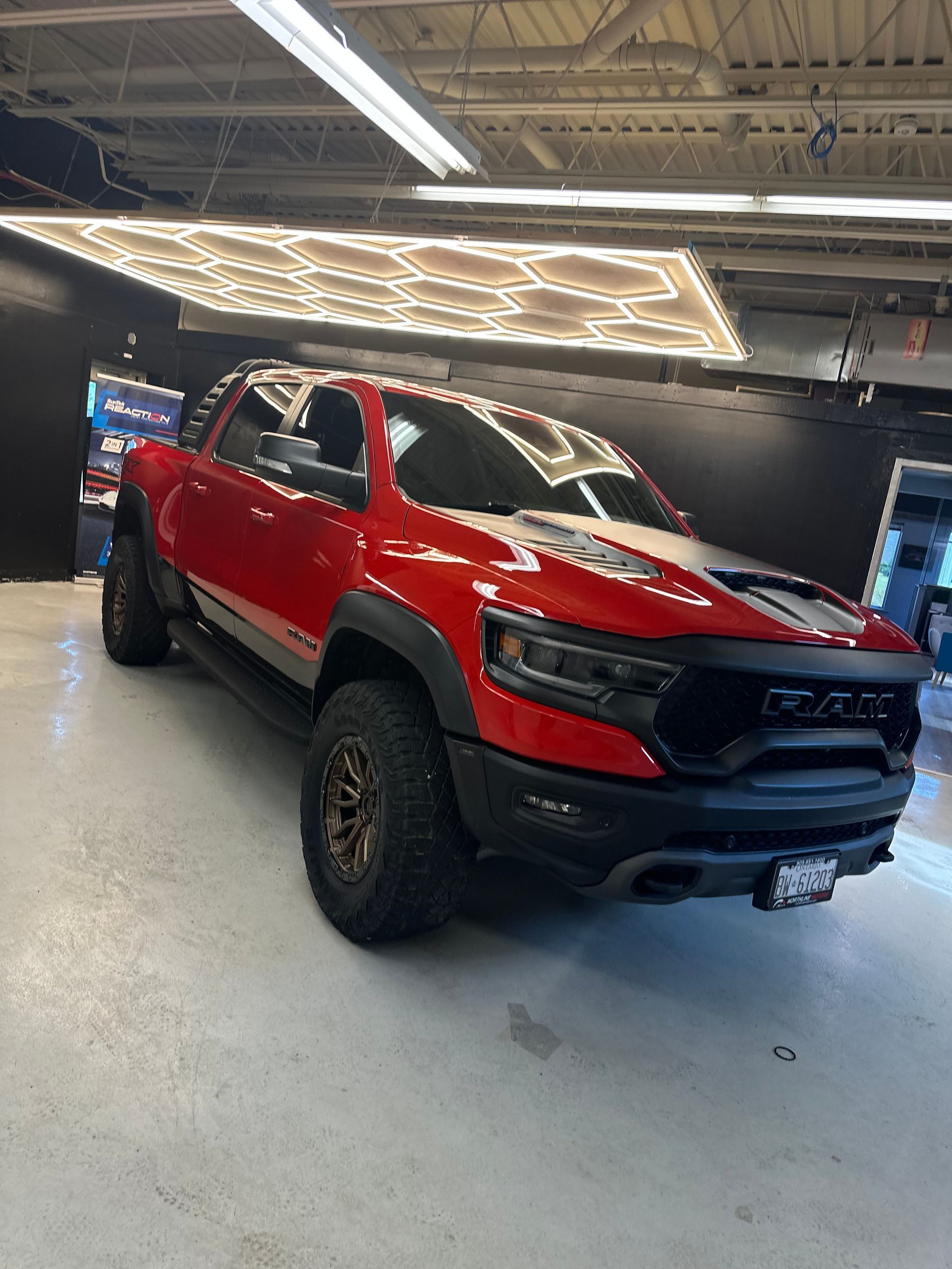 A red Ram TRX truck parked in a well-lit indoor garage with a geometric ceiling light fixture.