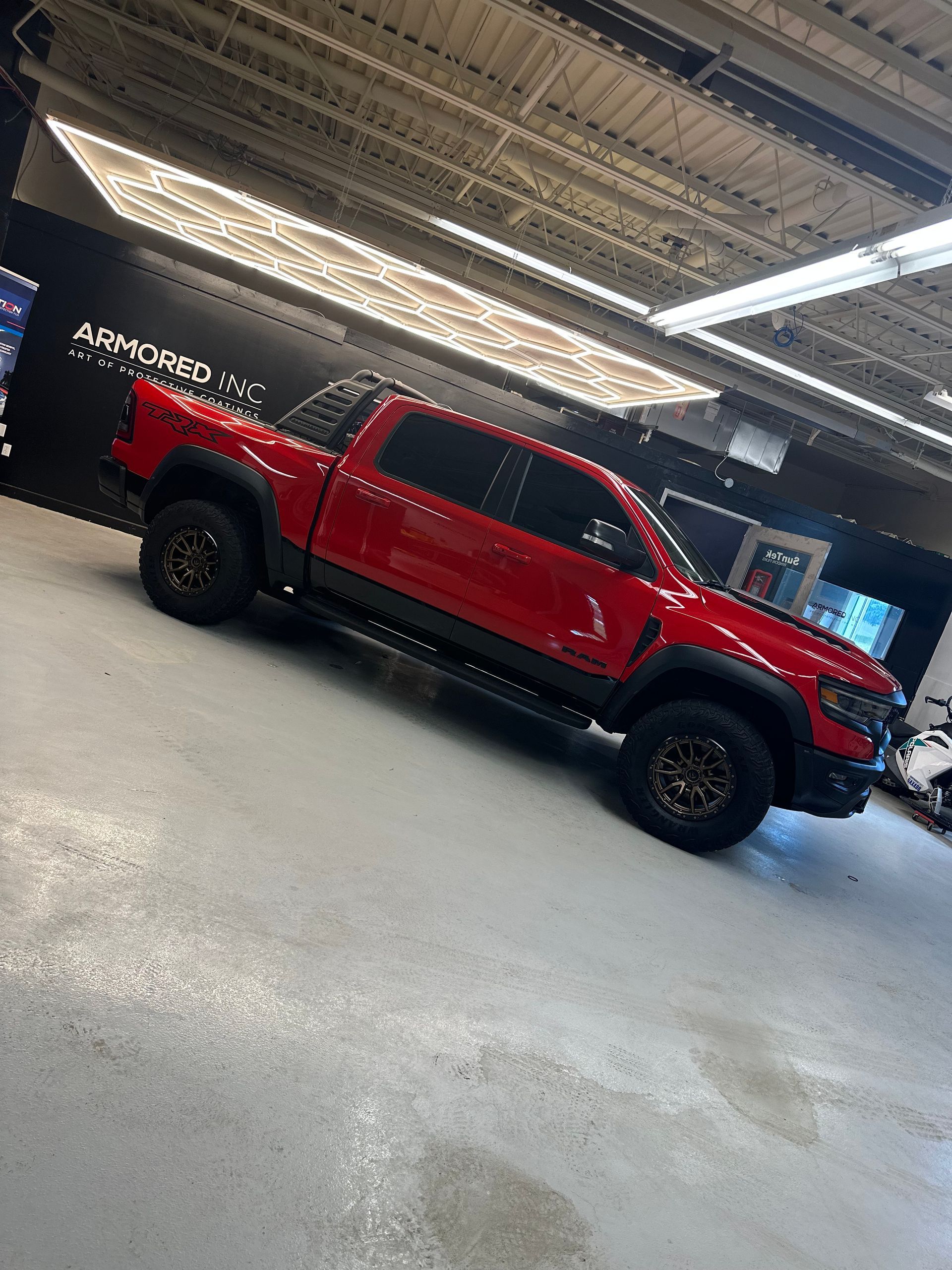 A bright red, off-road pickup truck parked inside a bright, industrial-style showroom with overhead lighting.