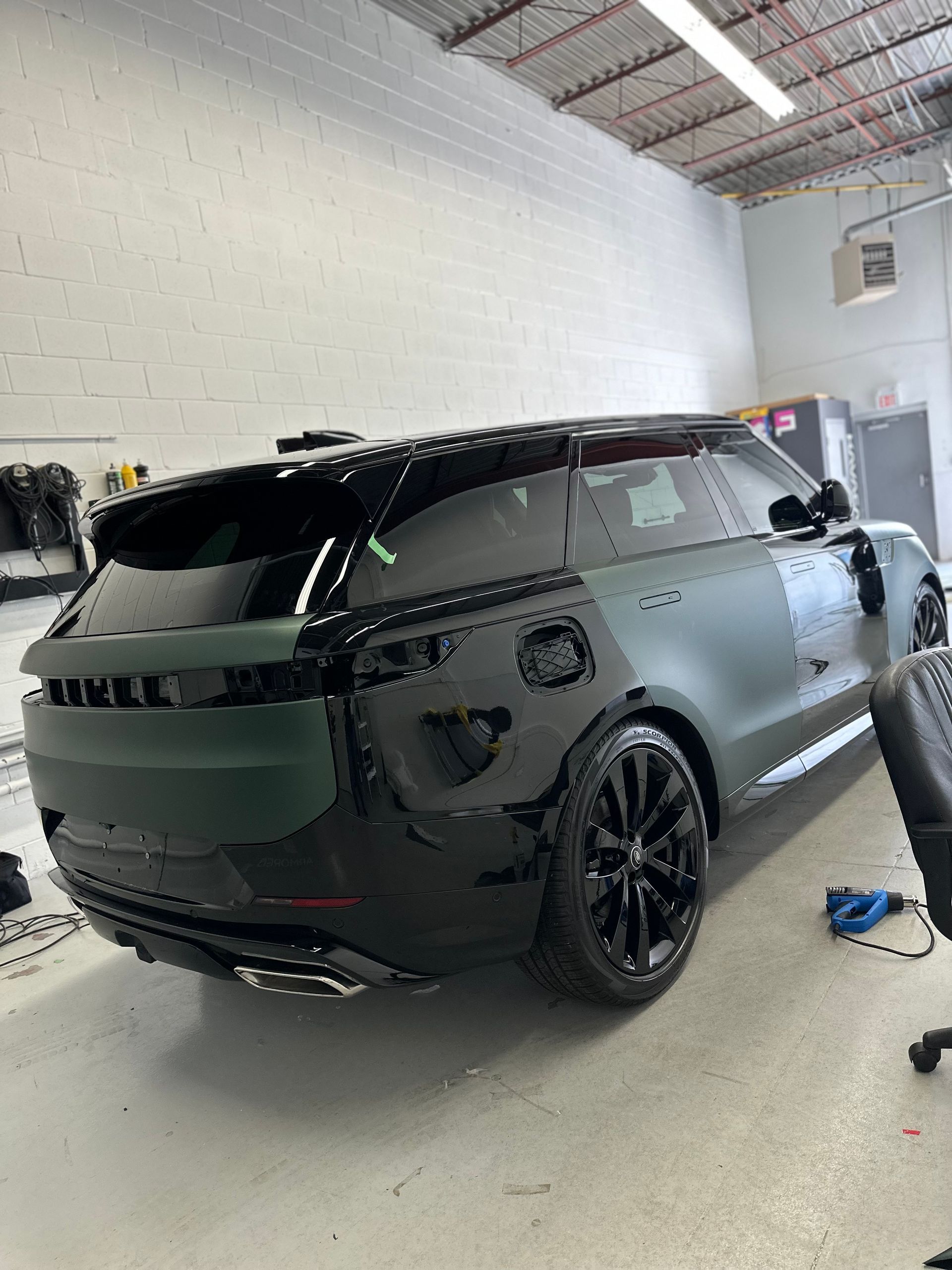 A black Range Rover in an auto shop undergoing a partial matte green vinyl wrap on the rear quarter panel and hatch.
