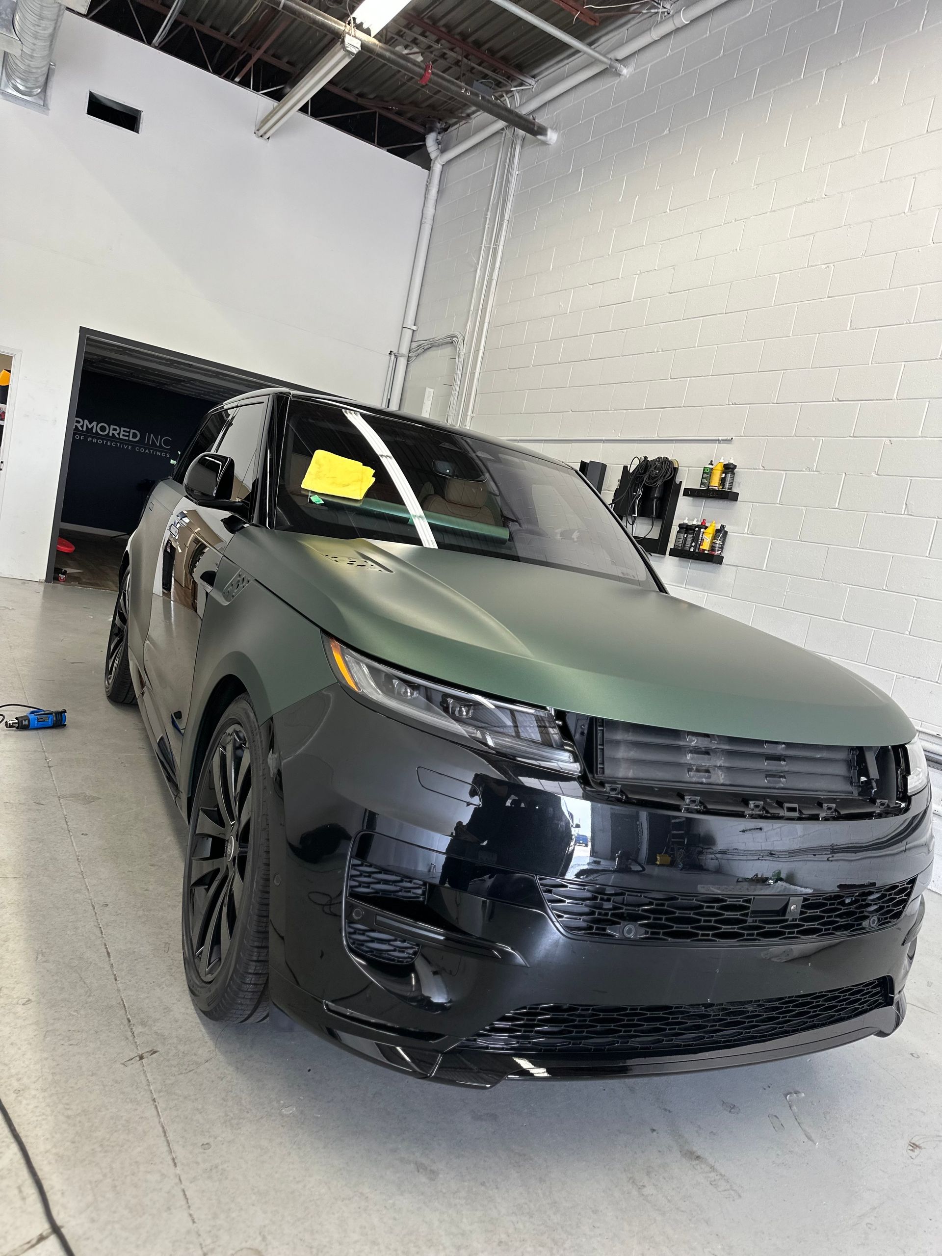A matte olive green and glossy black Range Rover Sport parked inside a well-lit automotive garage.