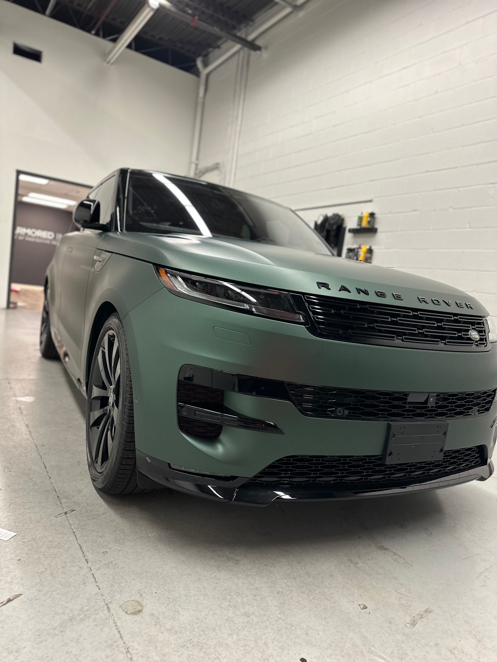 A matte olive green Range Rover parked inside a brightly lit garage or workshop.