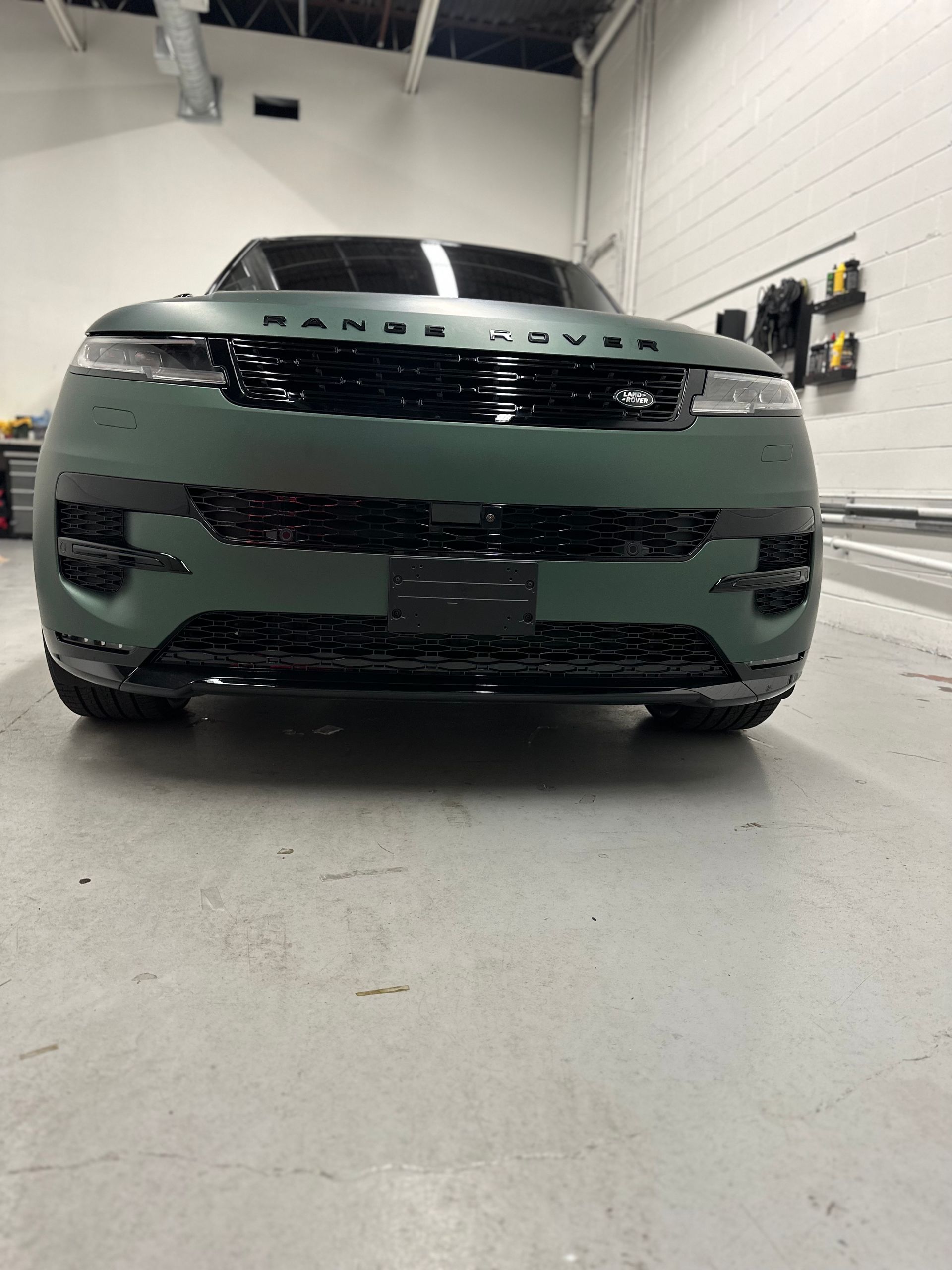 A matte olive green Range Rover parked inside a garage, viewed from the front.