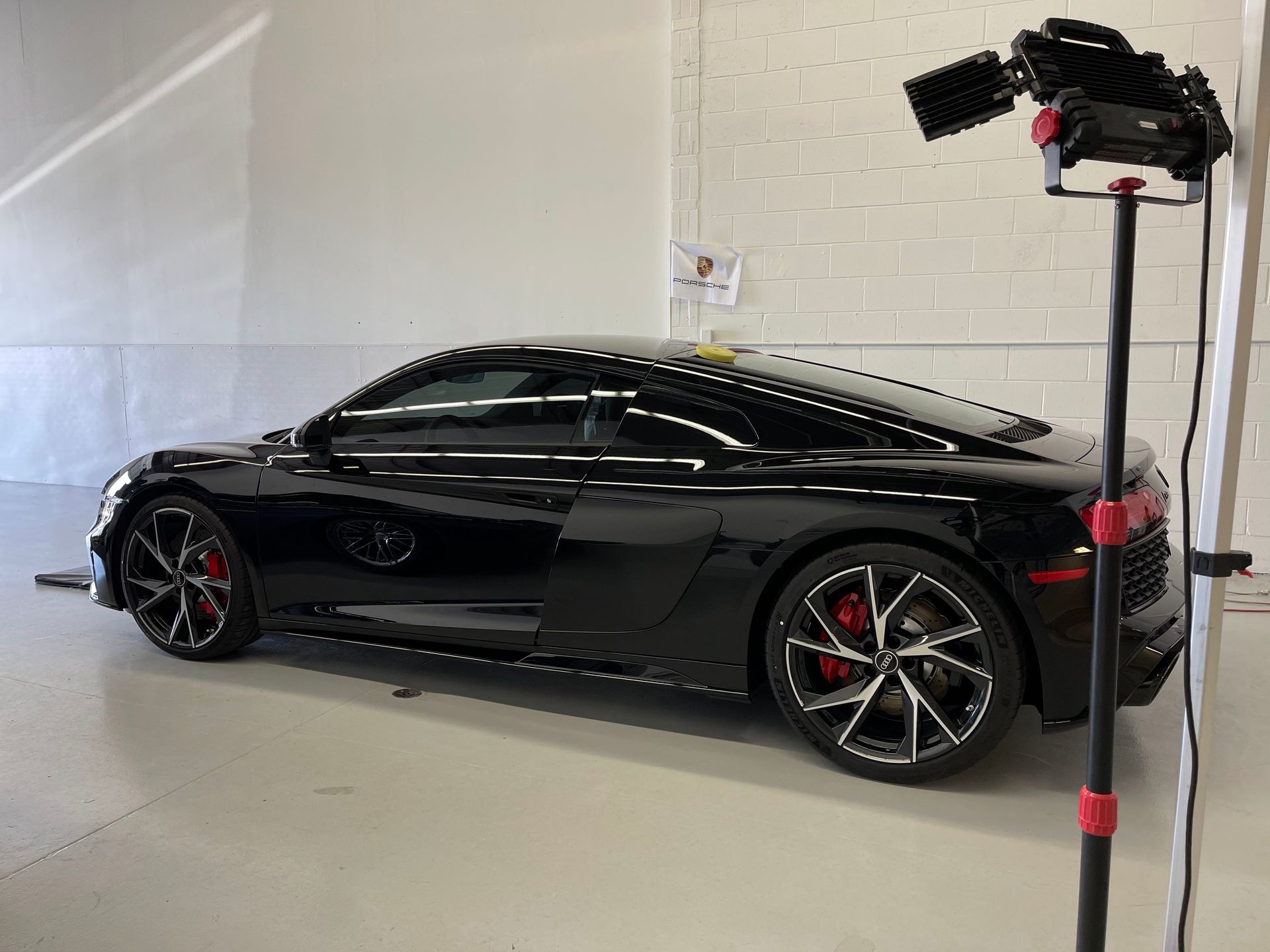 A sleek black Audi R8 parked in a white-walled studio next to a professional photography lighting stand.