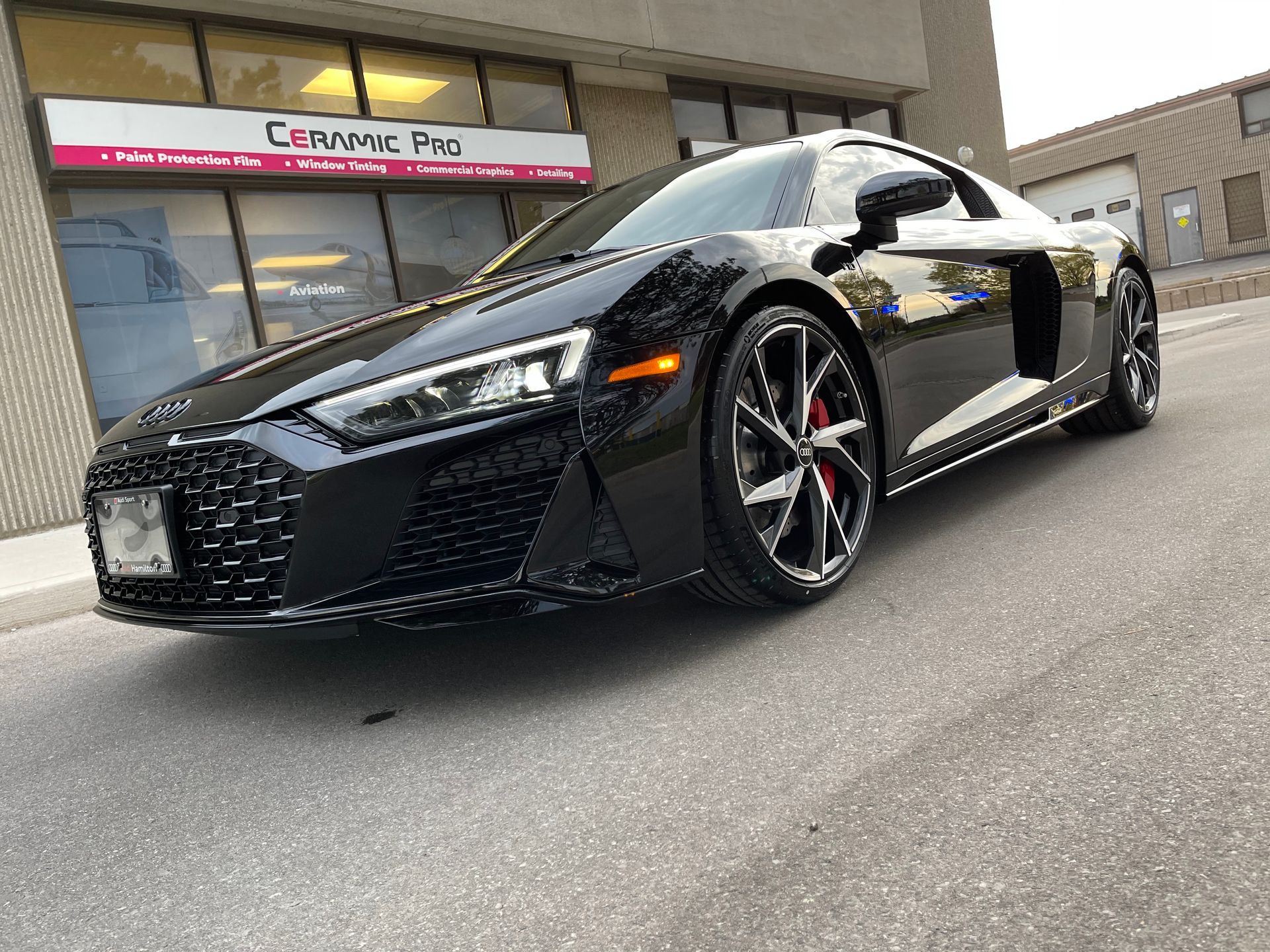 A sleek black Audi R8 sports car parked on an asphalt lot in front of a commercial building.