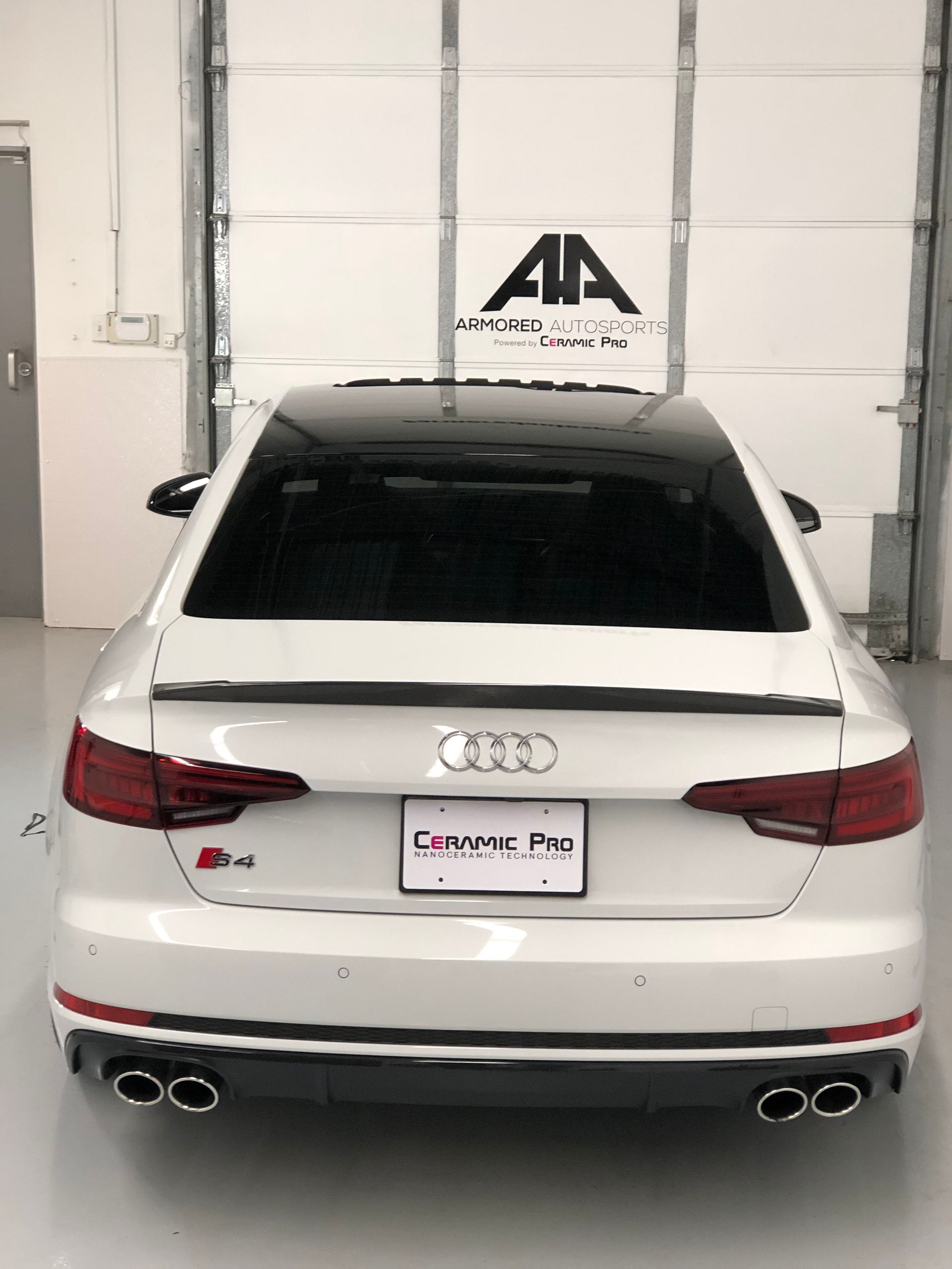 White Audi S4 sedan with a black roof and spoiler, shown from the rear in a garage.
