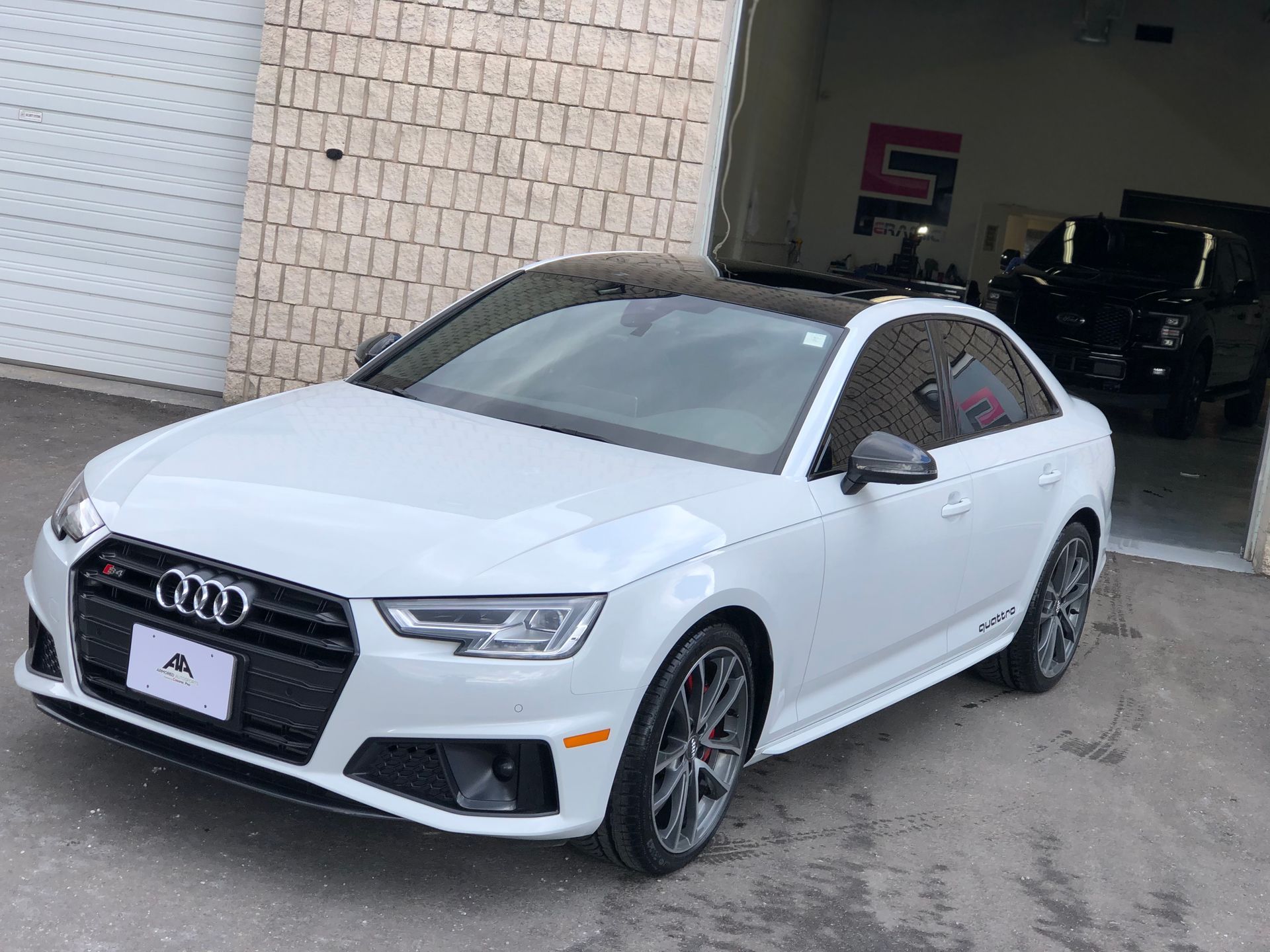 A white Audi S4 sedan parked outside a garage with a black roof and aftermarket wheels.