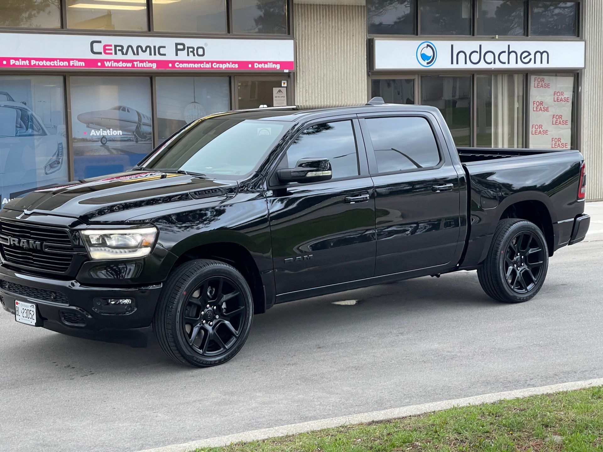 A black RAM pickup truck parked in front of a building with Ceramic Pro and Indachem signage.