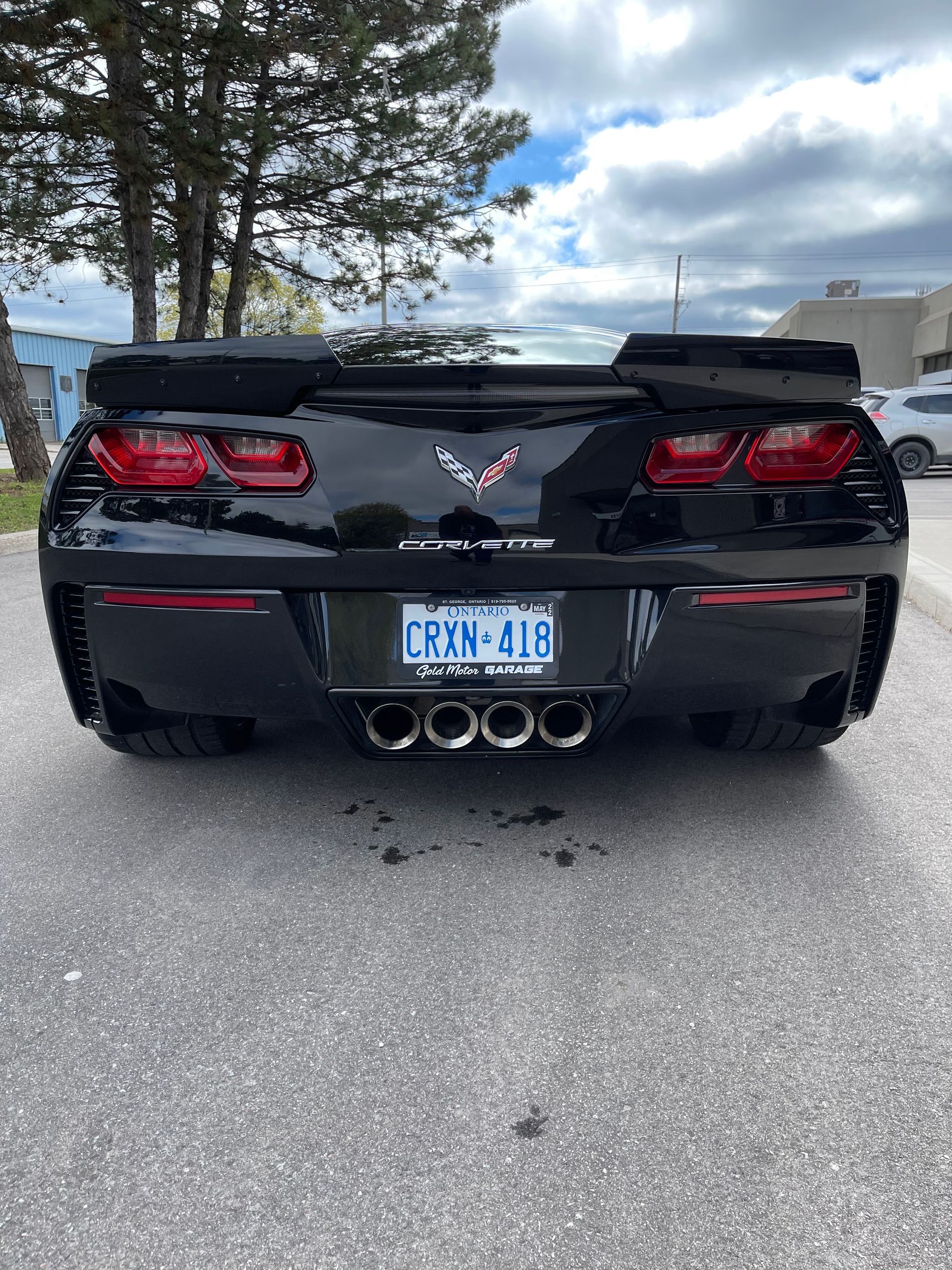 A black Chevrolet Corvette parked on an asphalt surface, viewed from the rear, showing its four exhaust pipes and emblem.