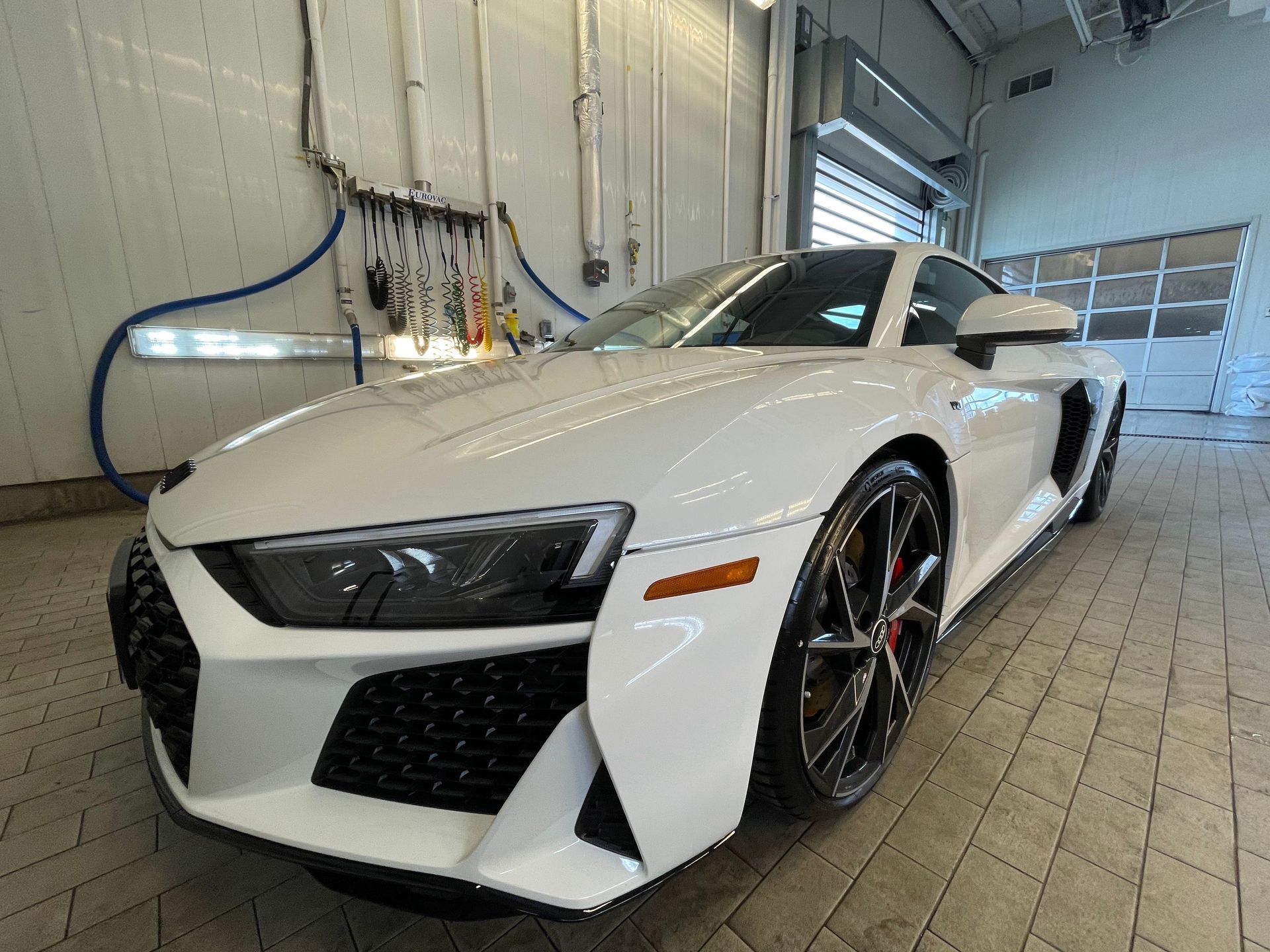 A white Audi R8 sports car parked on a tile floor in an indoor garage or service bay.