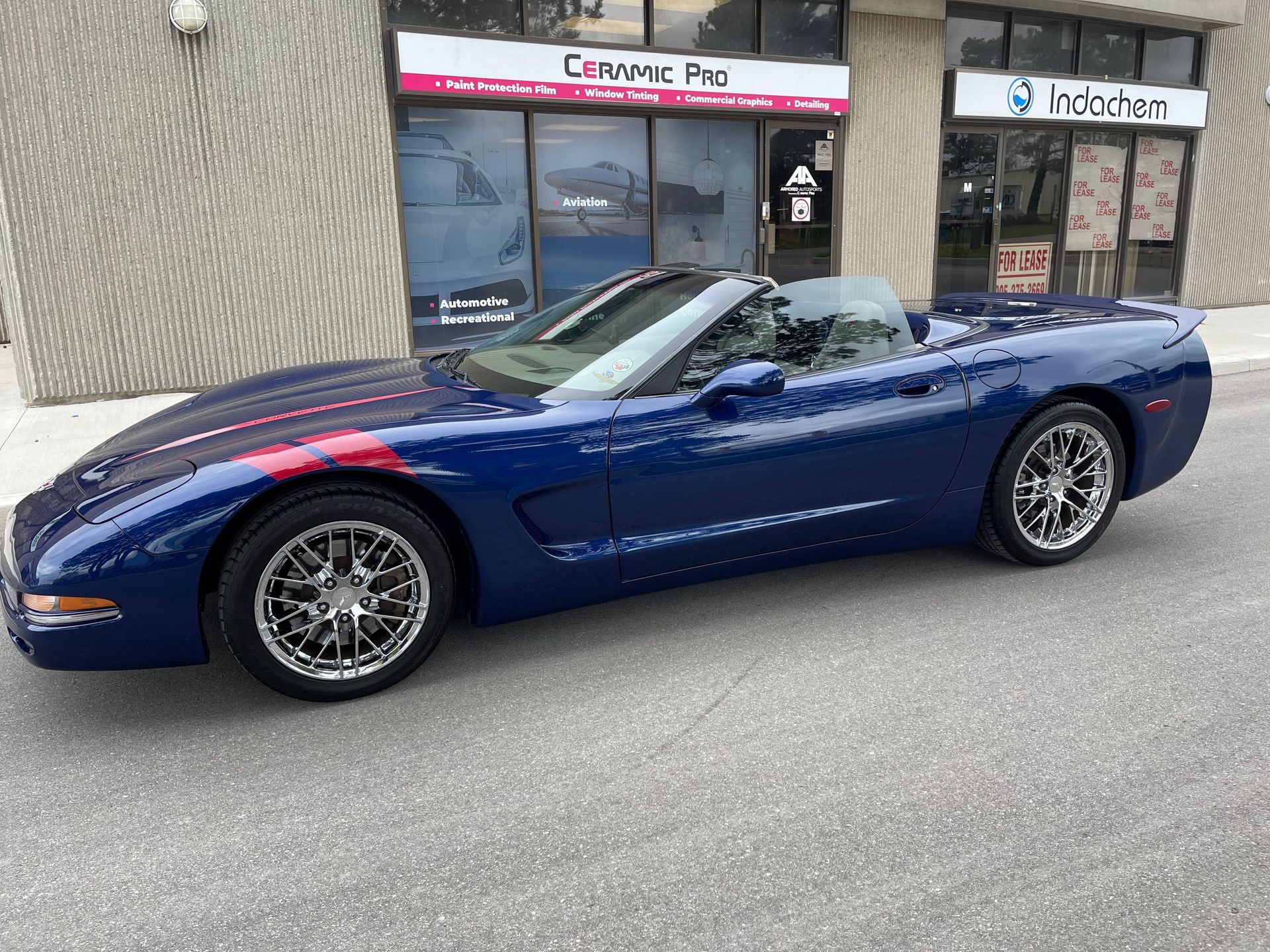 A blue C5 Chevrolet Corvette convertible parked in front of a Ceramic Pro automotive shop.