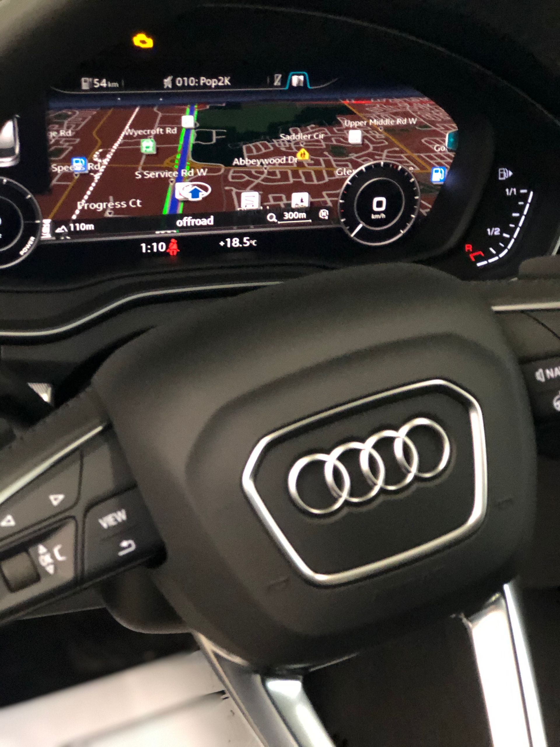 An Audi steering wheel featuring the brand logo, positioned in front of a digital dashboard displaying a navigation map.