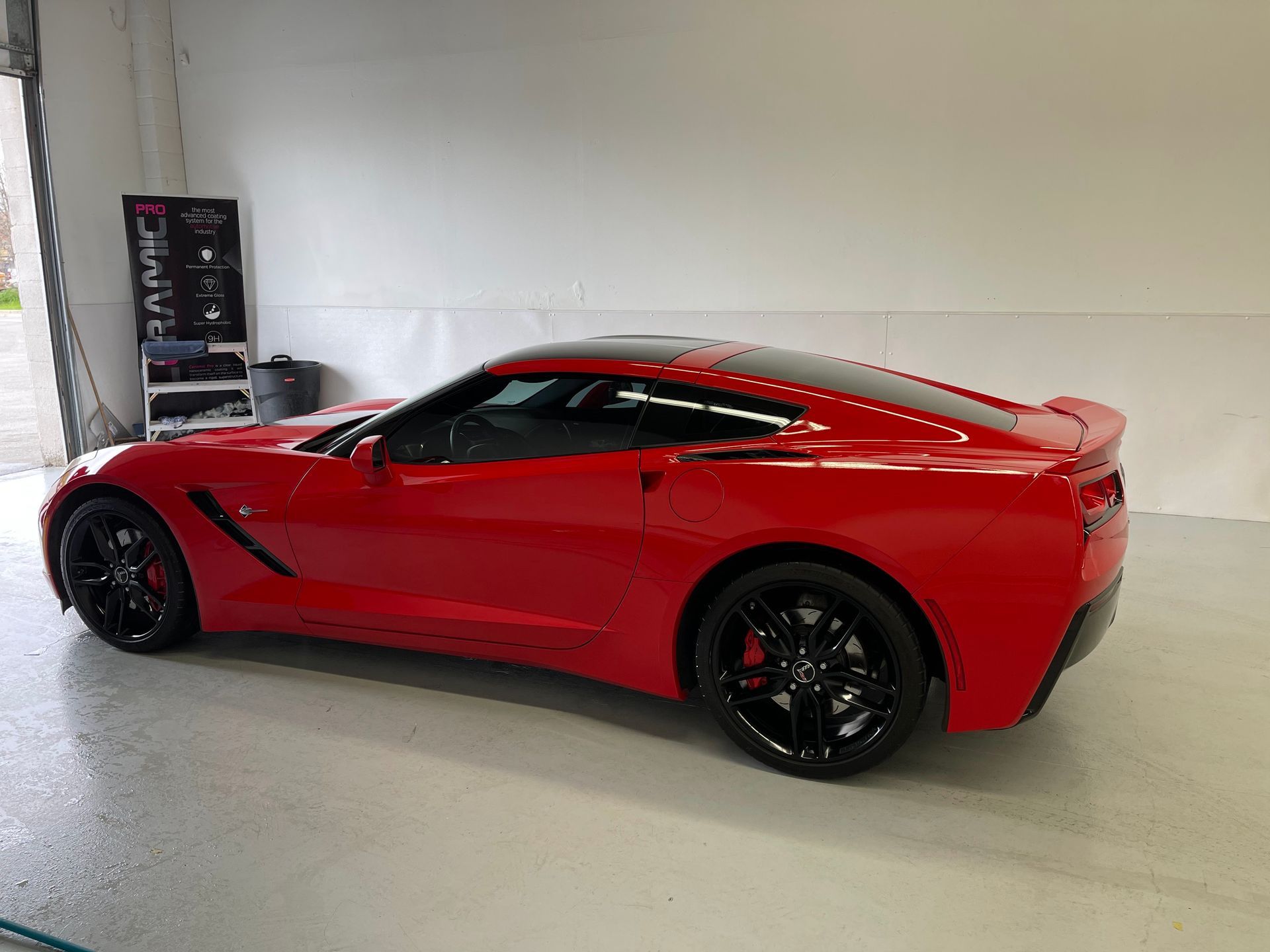 A red Chevrolet Corvette parked inside a bright, clean garage with black rims.