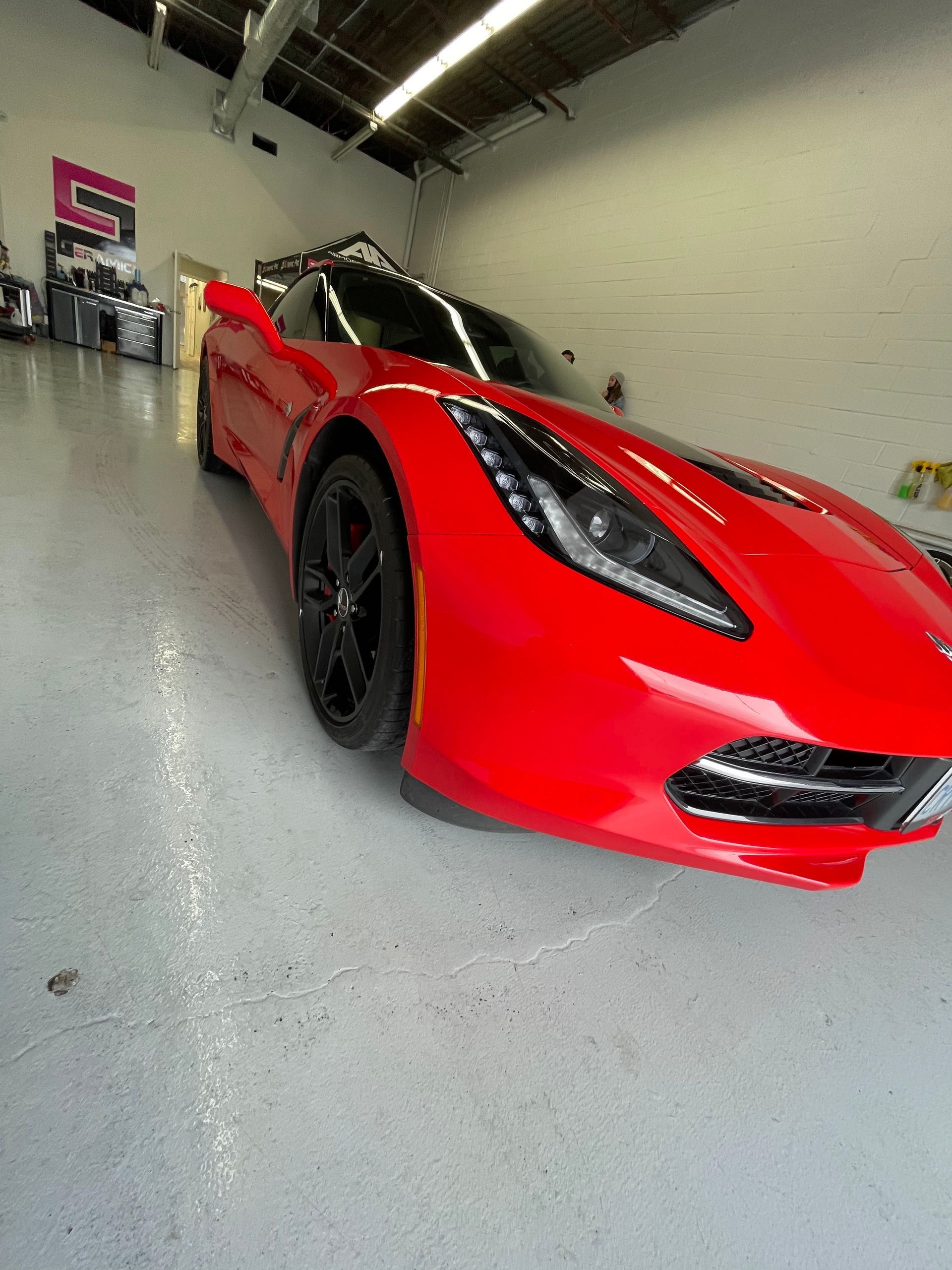 A vibrant red sports car with black rims is parked on a light grey concrete floor inside a brightly lit garage.