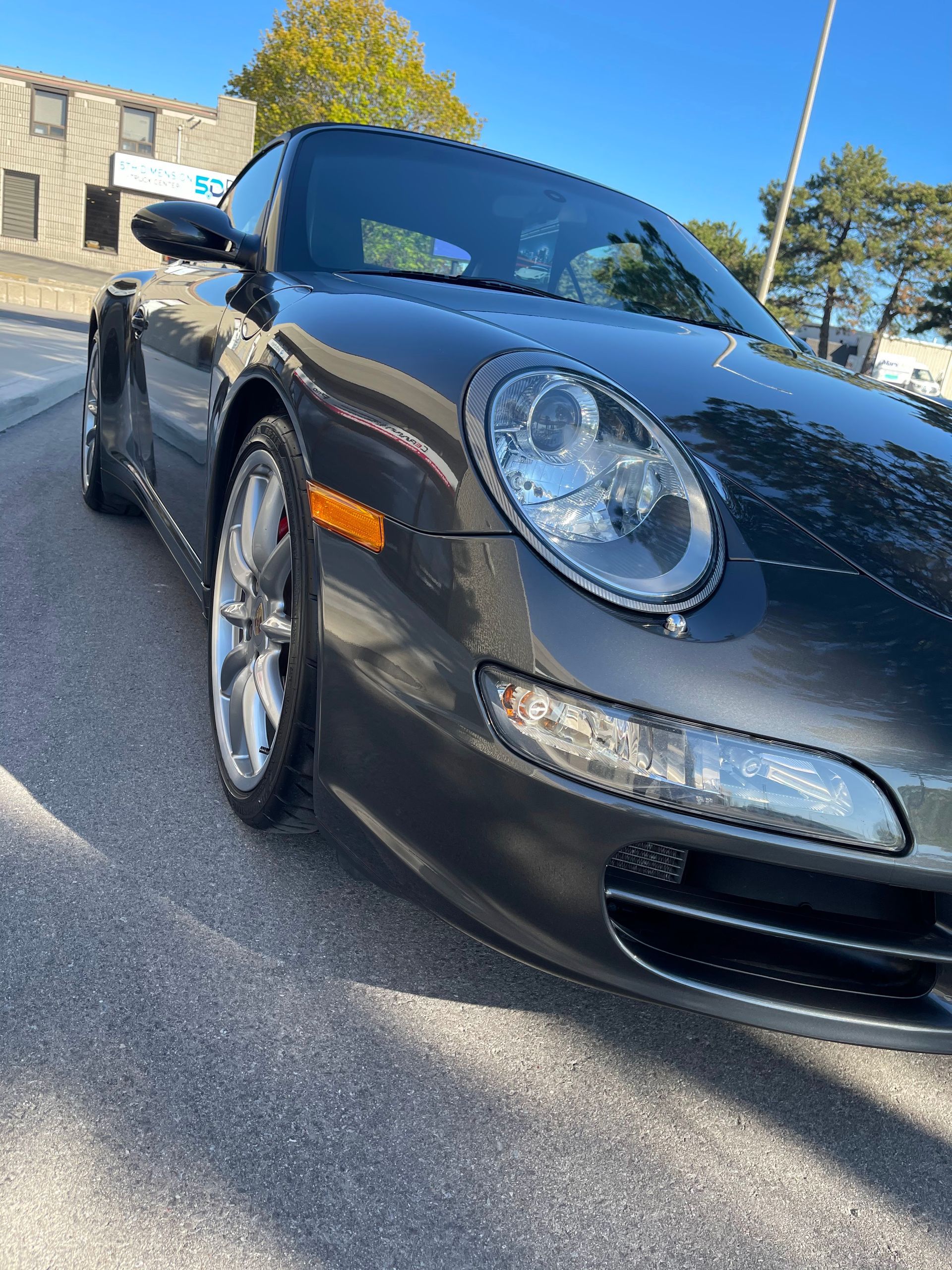 A sleek, dark gray Porsche parked outdoors on an asphalt surface under a clear blue sky.