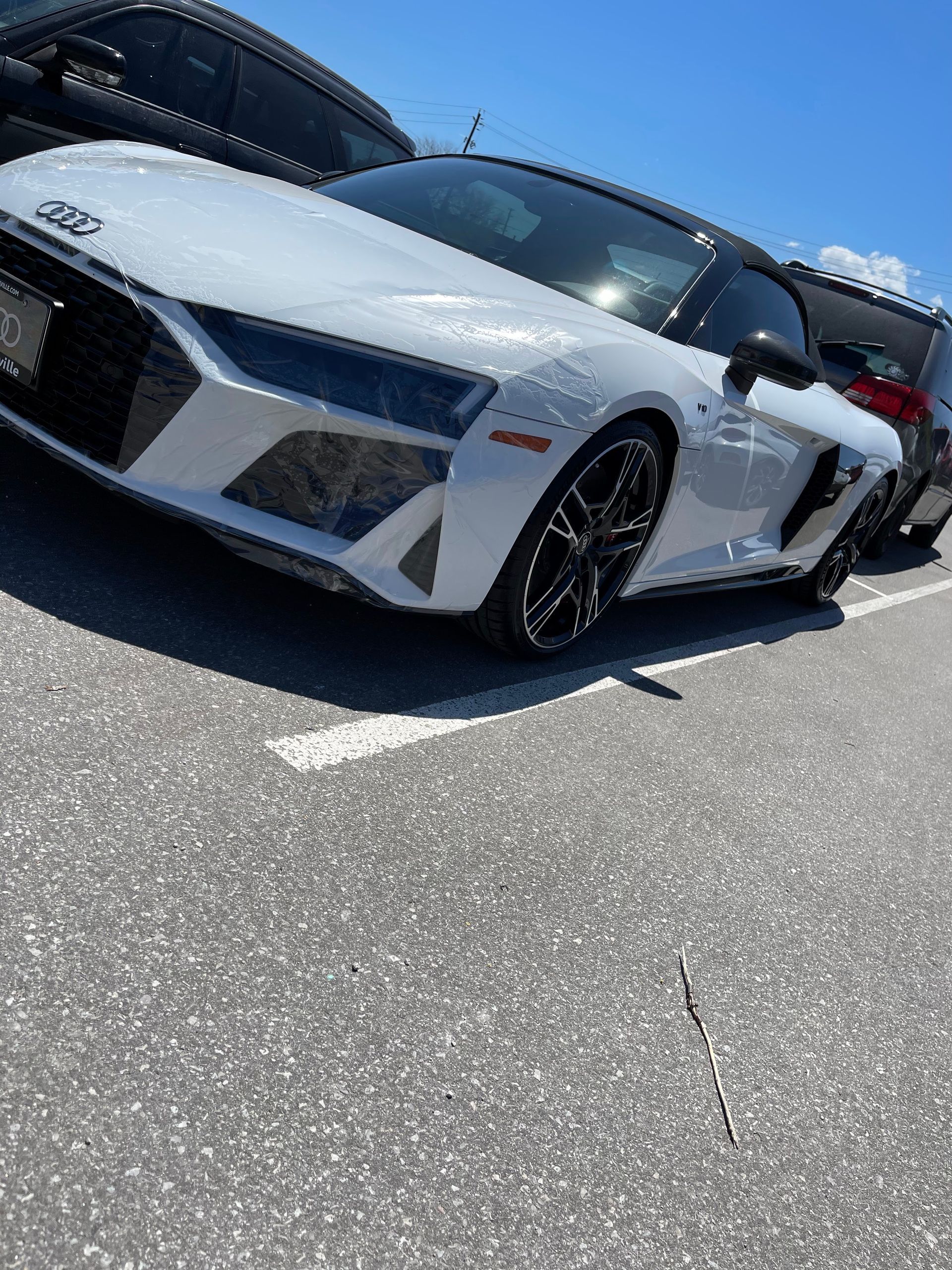 A white Audi R8 sports car parked in an outdoor asphalt parking lot on a sunny day.