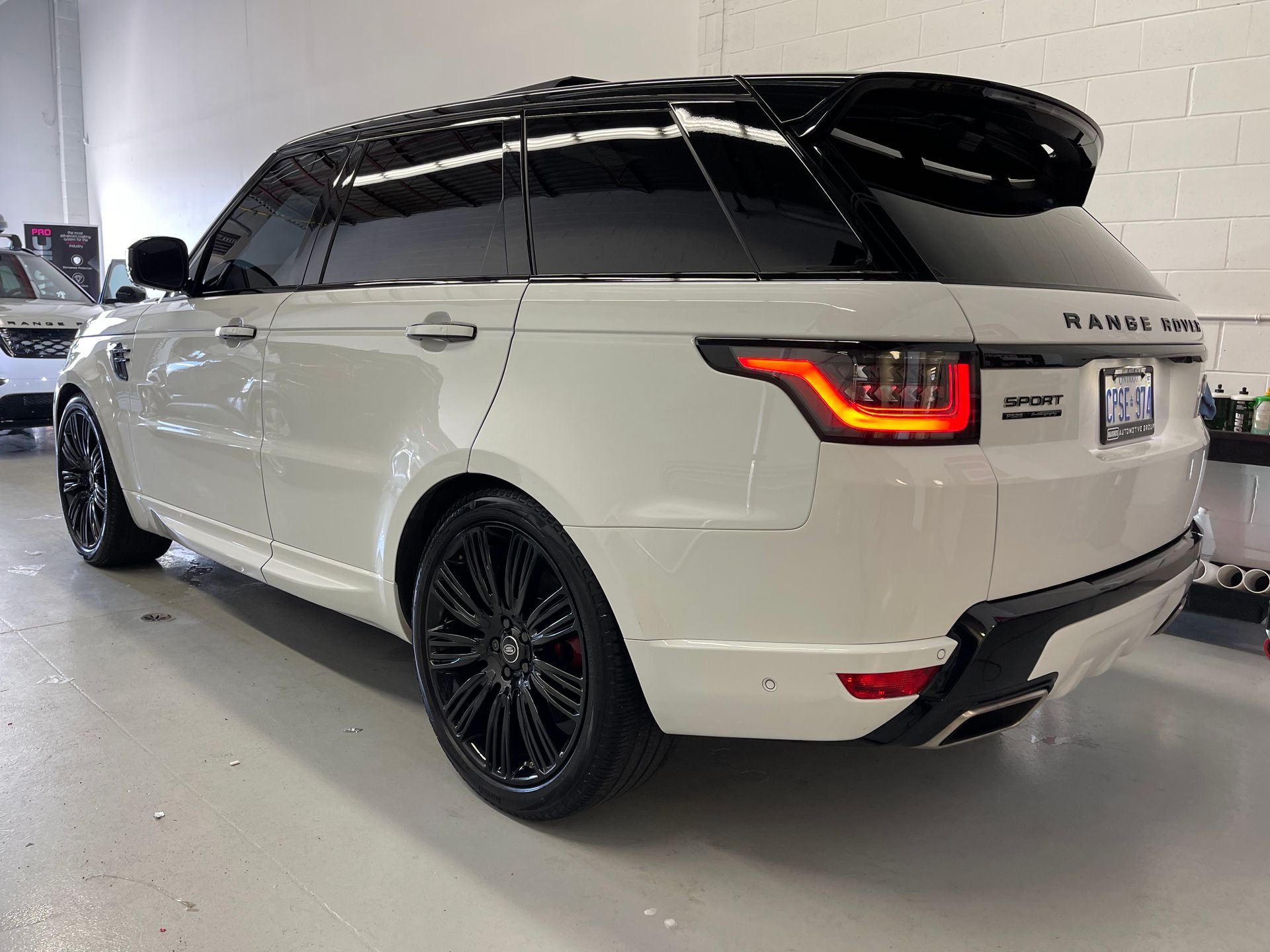 A white Range Rover Sport with black wheels and a black roof, parked inside a garage.