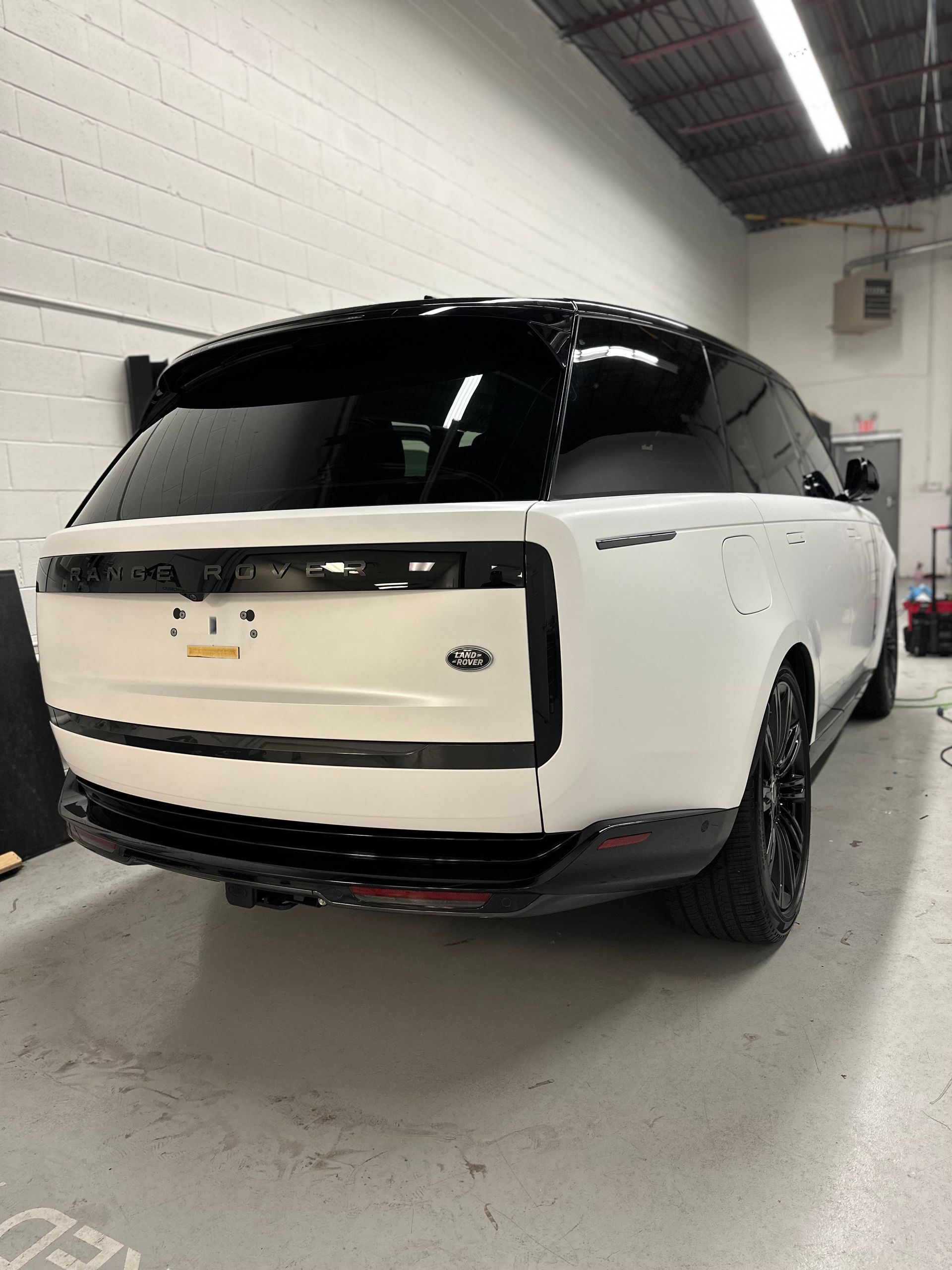 Rear angle view of a white Land Rover Range Rover with a black roof and black wheels parked inside a garage.