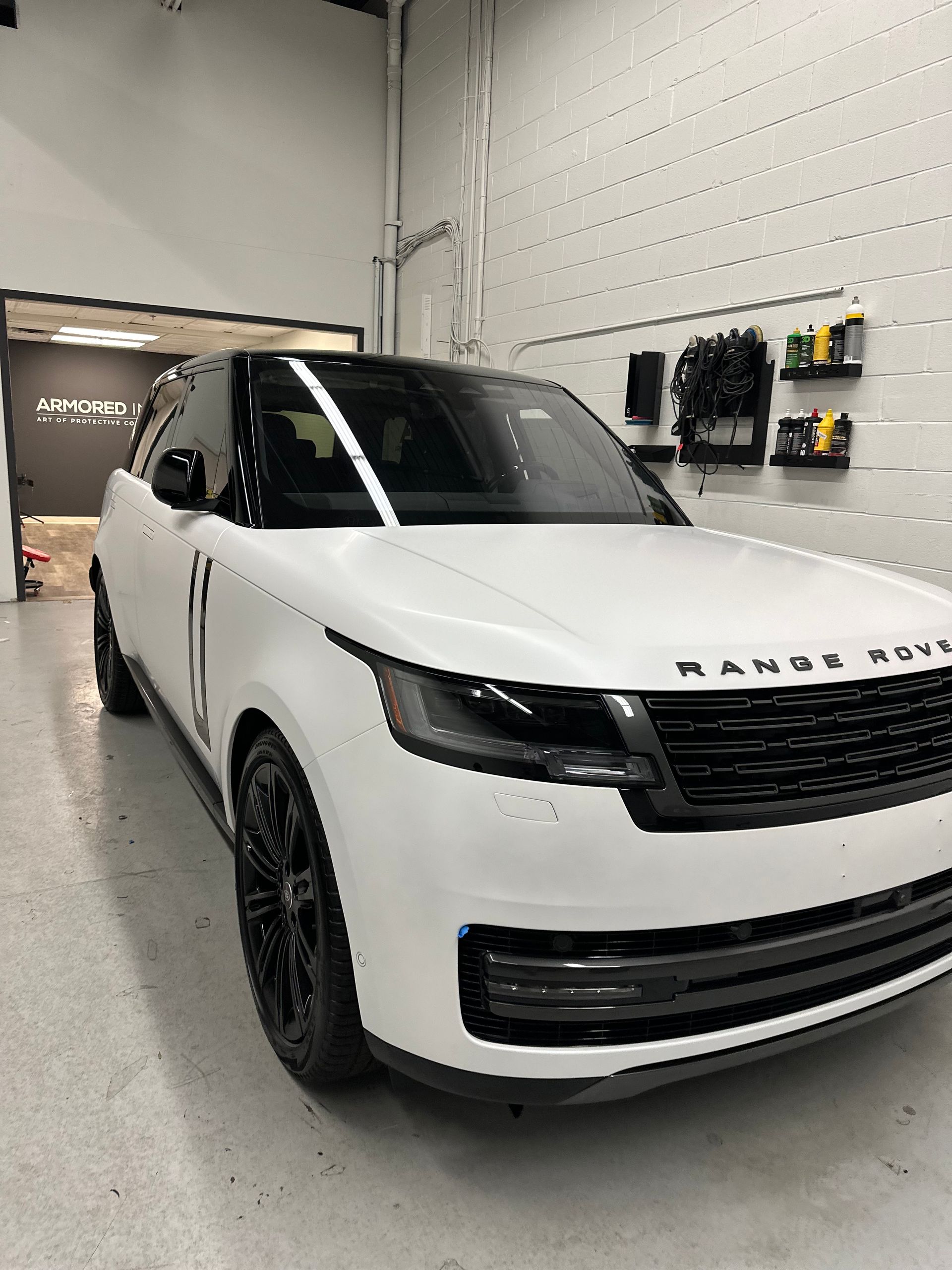 A white Range Rover with a black roof and black wheels parked inside a brightly lit garage.
