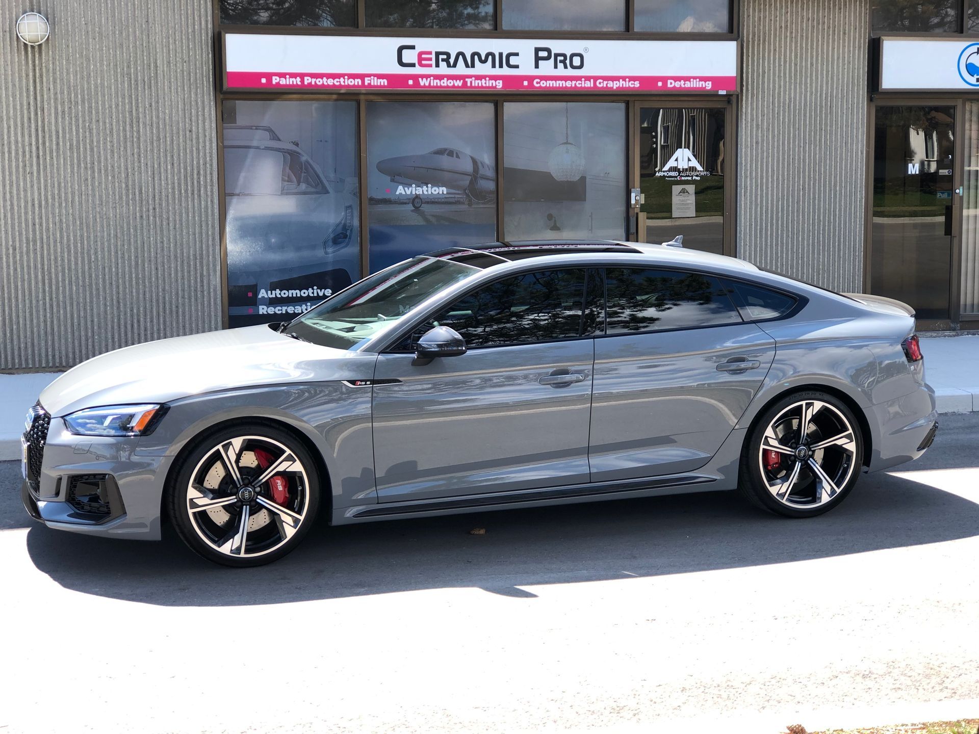 A Nardo gray Audi S5 Sportback parked in front of a Ceramic Pro shop.