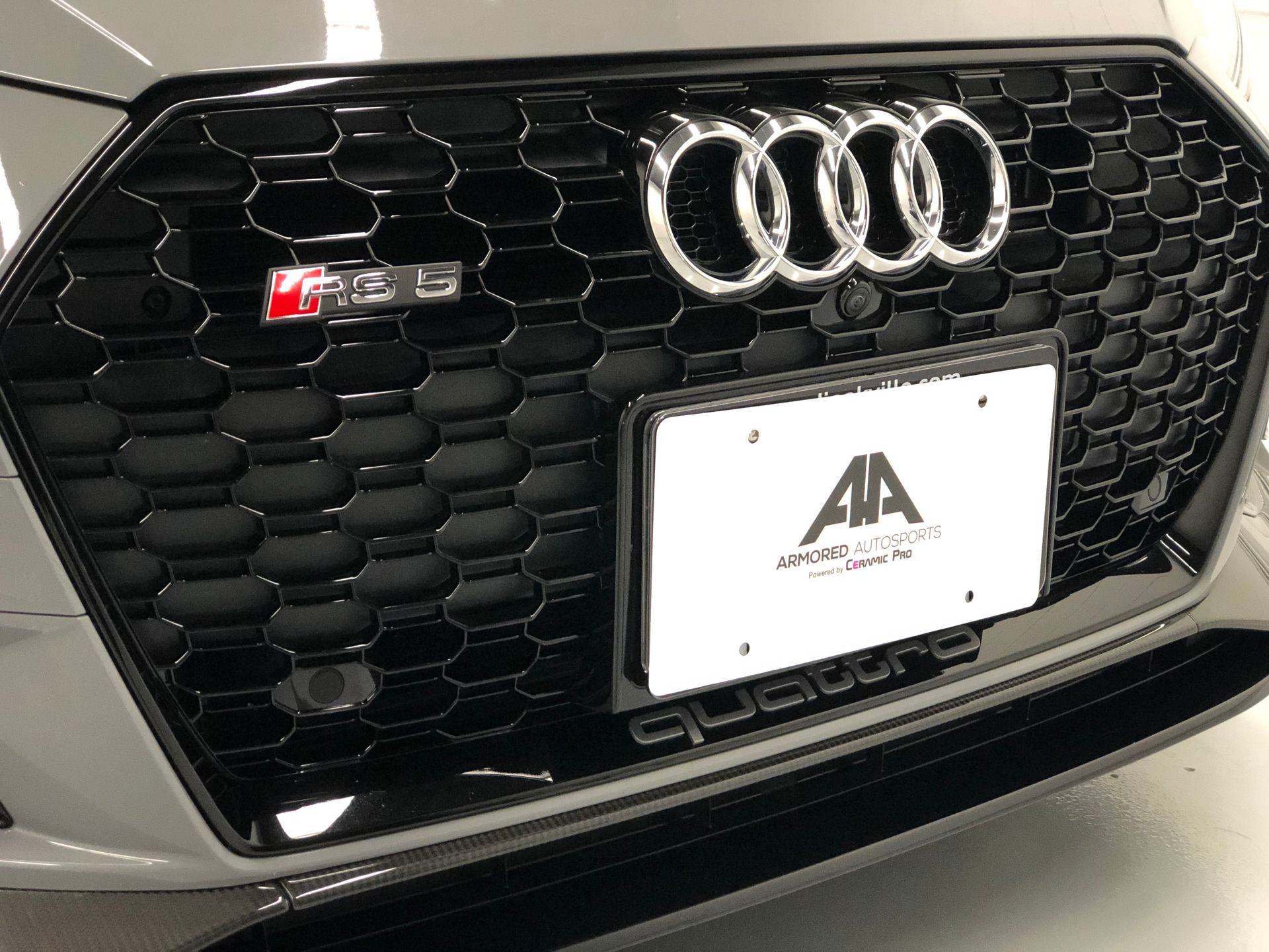 Close-up of a grey Audi RS3 front grille featuring the brand logo, an RS3 badge, and a dealership license plate frame.