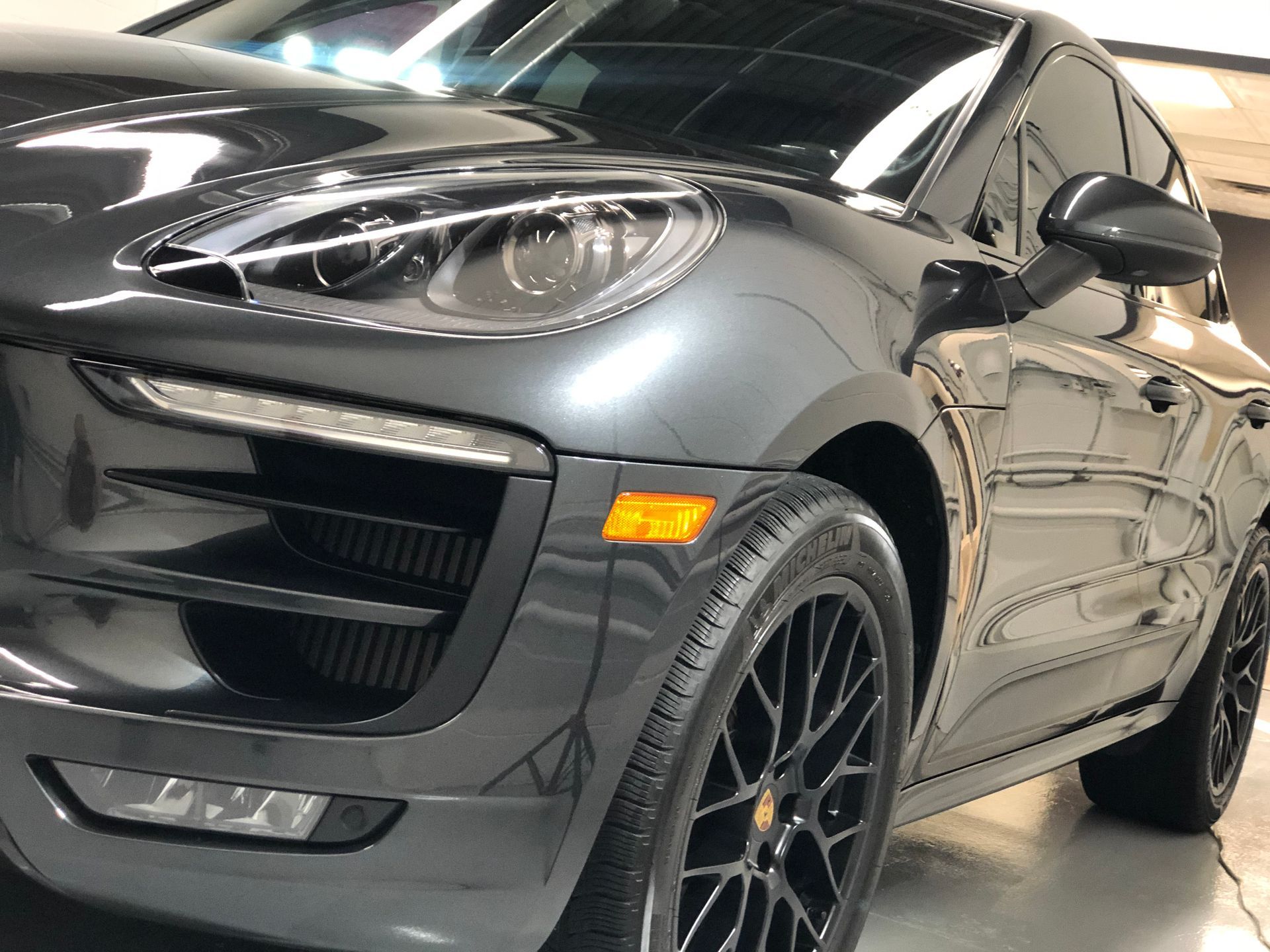 A close-up, low-angle view of the front quarter of a dark grey Porsche Macan in a garage with polished concrete floors.