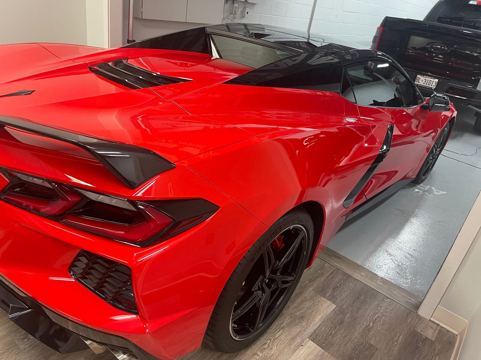 A bright red Chevrolet Corvette C8 convertible parked inside a garage with black wheels and trim.